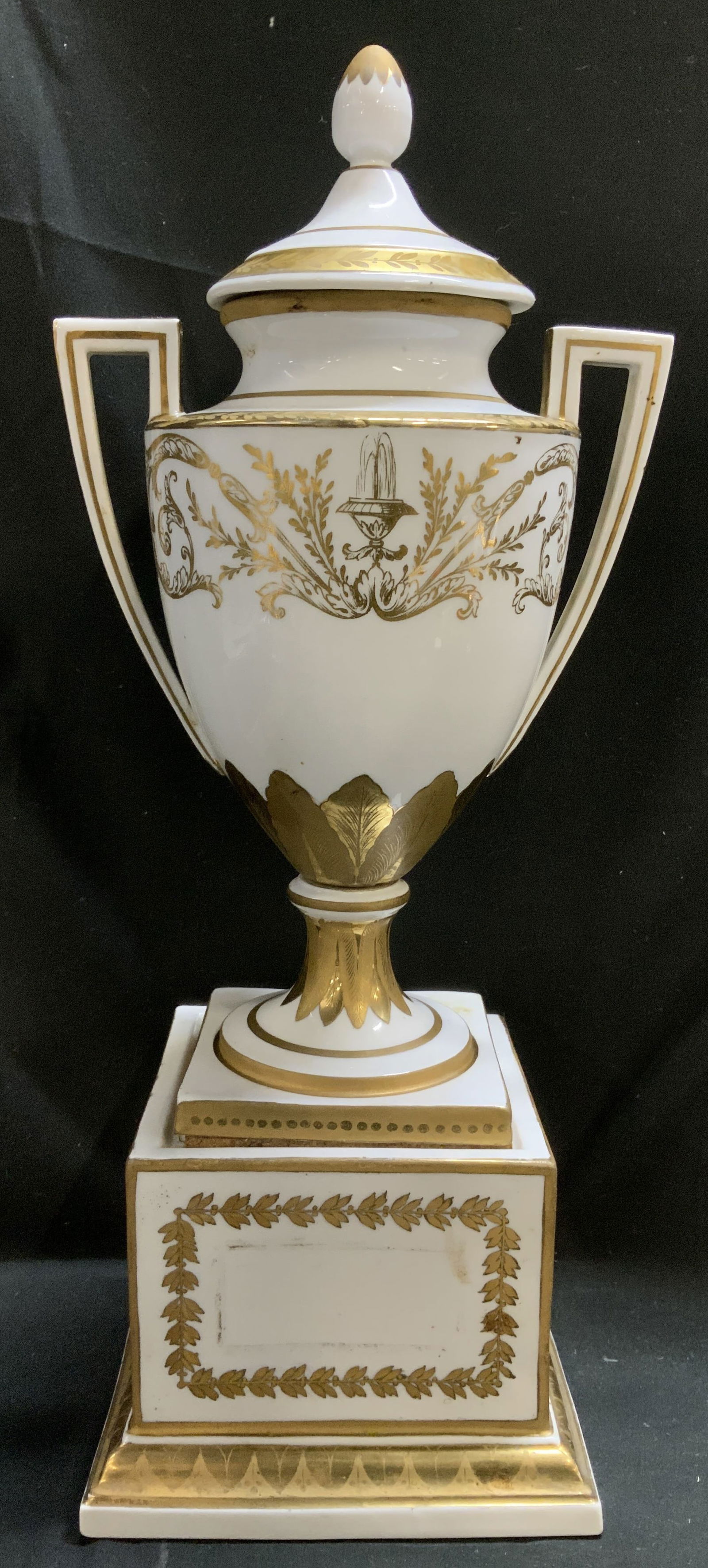 Antq Signed Neoclassical Gilt Porcelain Lidded Urn: Piece is antique signed and trademarked on underside. Piece is porcelain & is mounted on a pedestal base. Piece has hand-painted gilt accents, laurel leaf borders & floral motifs. Lid is topped w fini