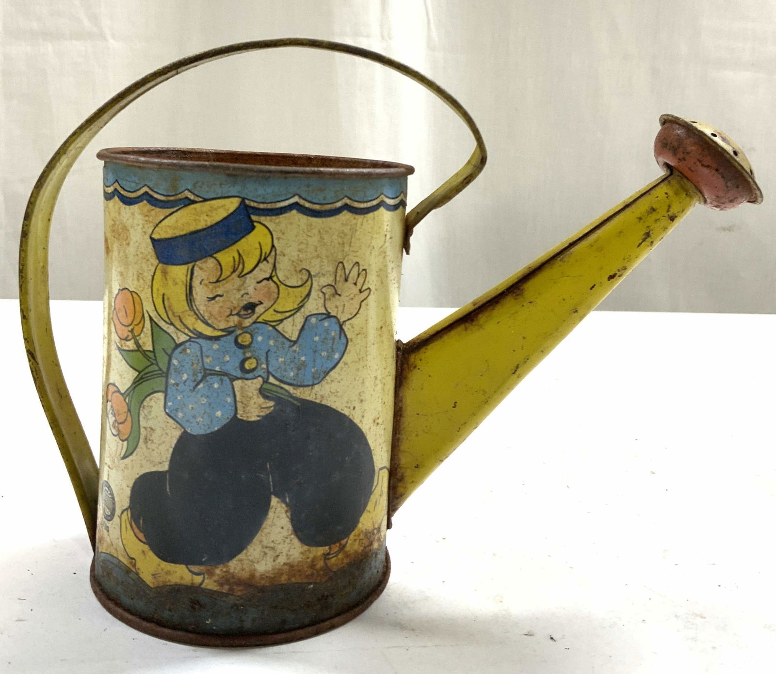 OHIO ART Vtg Lithographed Watering Can Toy: Watering can toy appears to be OHIO ART. Piece is vintage. Watering can crafted from tin. Piece depiction of female figure holding flowers and another female figure watering plants. Vessel measures ap