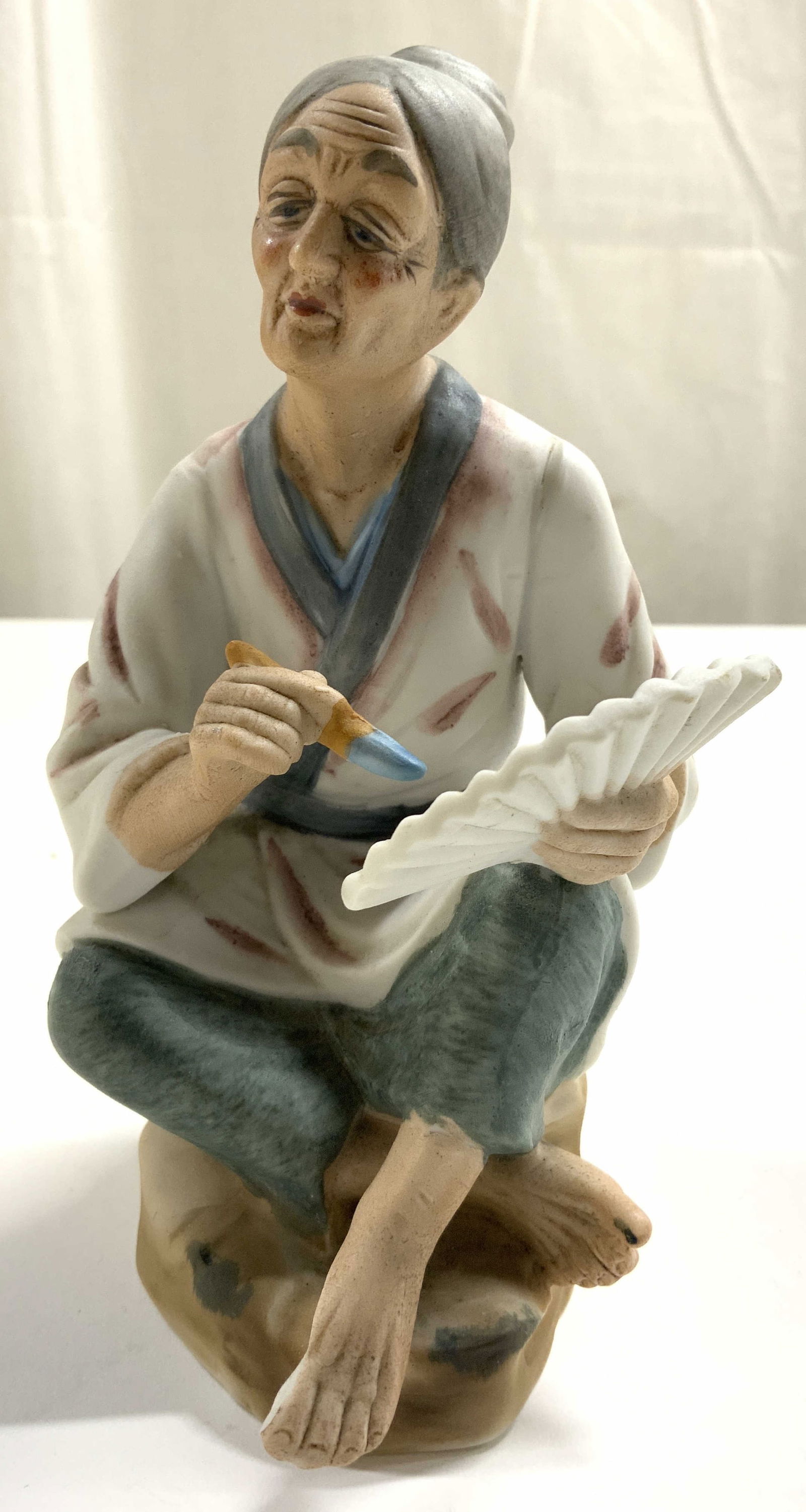 Asian Art Serv-Ware by Rubel Jpn Fig Porc W Fan: Asian Art Serv-Ware by Rubel Japan Old Woman Figurine Porcelain Painting Fan. Piece depicts an elderly female figure seated cross legged painting a hand fan. Appears to have some hand painted elements