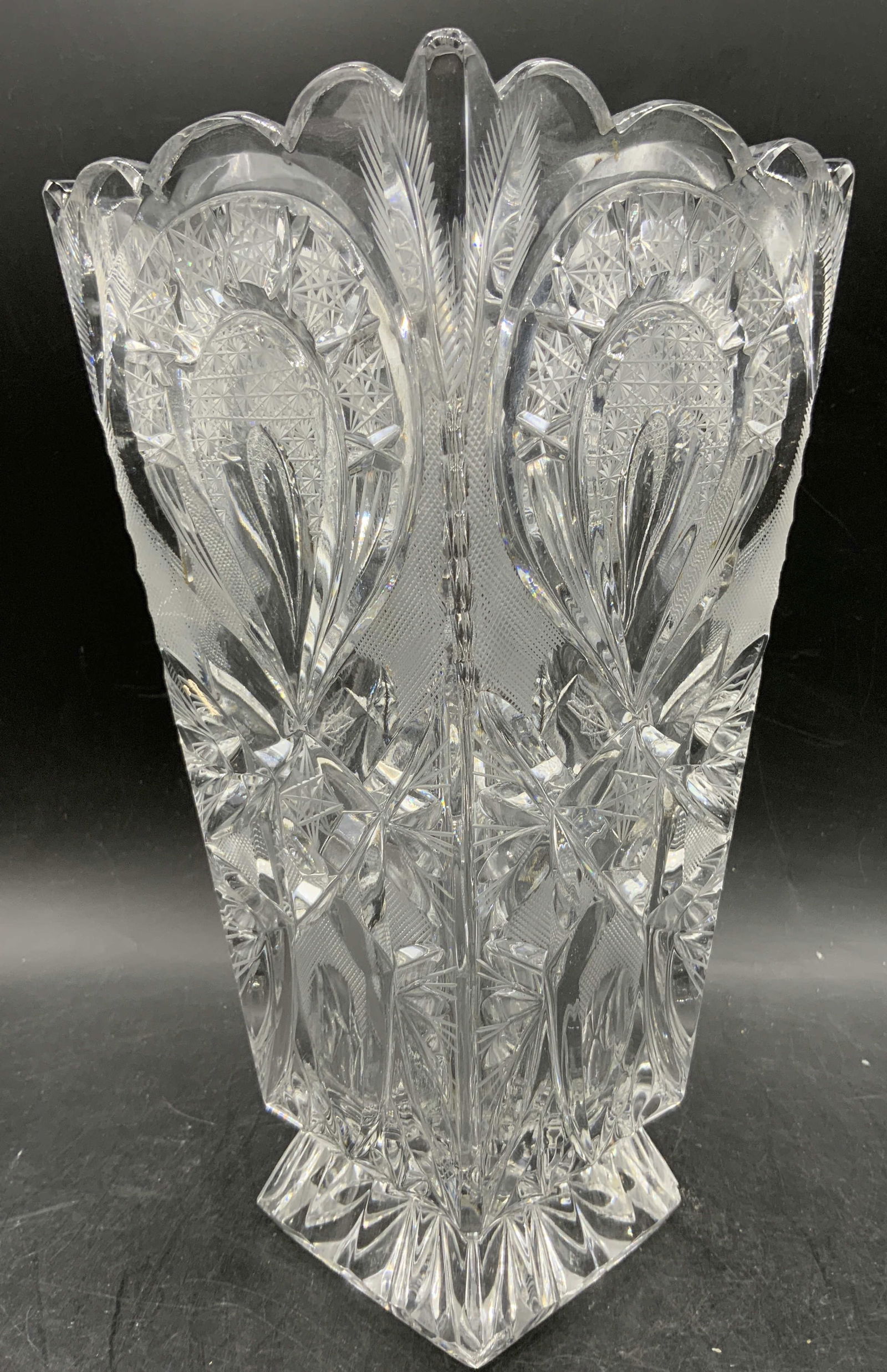 Cut Crystal Hobstar Motif Footed Vase: Vase is cut crystal. Piece has hobstar motif and geometric relief detail. Vase is footed. Piece has round toothed rim. Measures approximately 11 inches tall 5.5 inches wide and deep. Vase, cut crystal