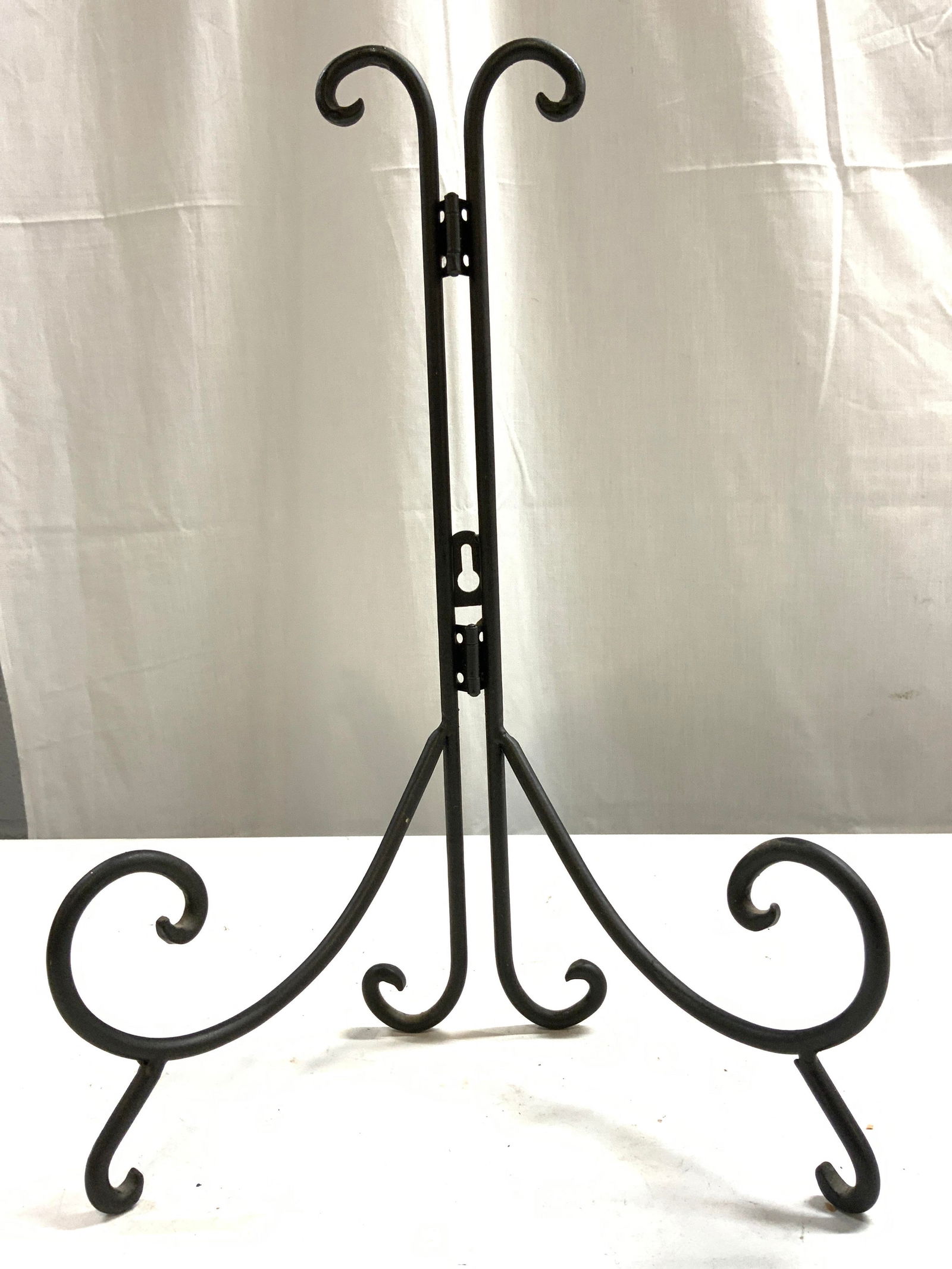 Vntg Folding Curled Wrought Iron Easel: Easel is vintage. Piece is black toned appears to be wrought iron. Easel has curled feet. Top of piece also has curled structures. Easel folds. Easel measures approximately 14 inches tall 9 inches wid
