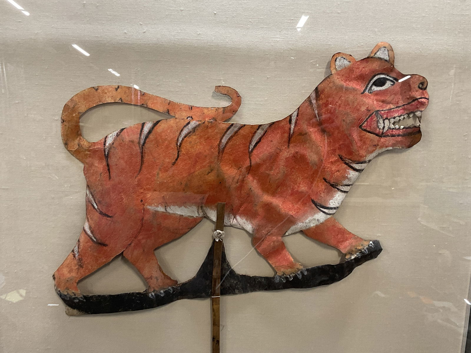 Mounted Wayang Kulit Tiger Shadow Puppet: Mounted Wayang Kulit shadow puppet. Tiger. Hand painted. Material unknown, possibly leather. Mounted on canvas under acrylic. Not examined out of acrylic cover. Total dimensions approx 24 x 27 inches.