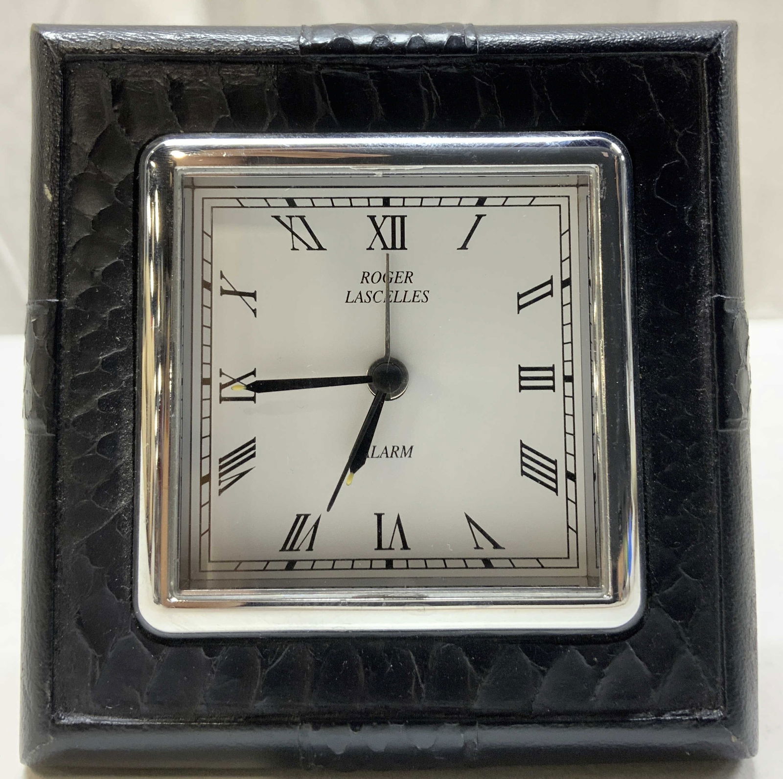 ROGER LASCELLES Faux Leather Alarm Clock ENGLAND: ROGER LASCELLES Faux Leather Alarm Clock ENGLAND Alarm clock has a black faux leather textured case. Clock has Roman numerals & operates on a Quartz movement. Signed & marked. Reads ROGER LASCELLES. C