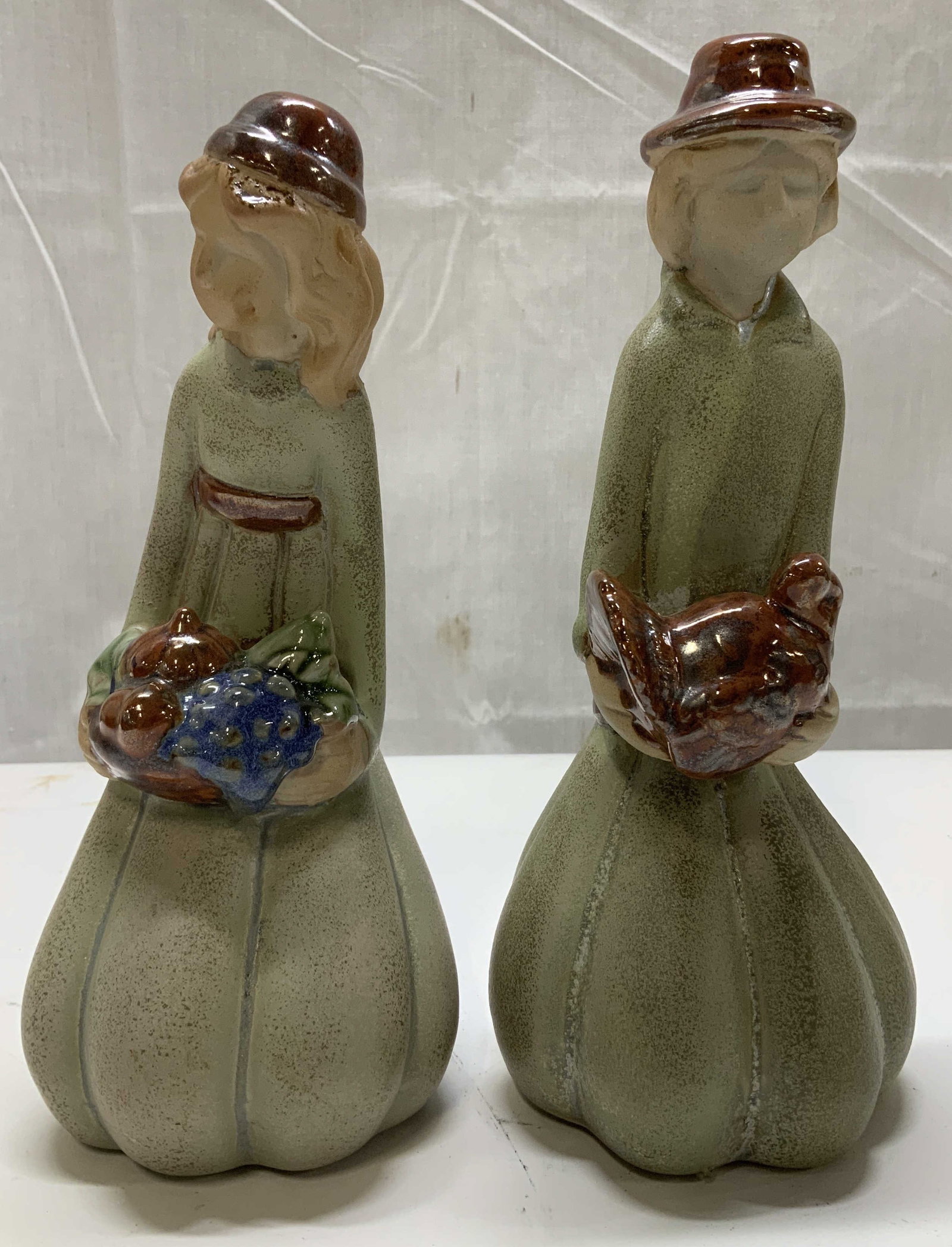 Pair Vntg Thanksgiving Pilgrim Man & Woman Figs.: Pair of Thanksgiving pilgrim figurines. Man & woman are dressed in traditional pilgrim attire. The woman figurine is holding a basket with what appears to be fruit and vegetables. The man figurine is 