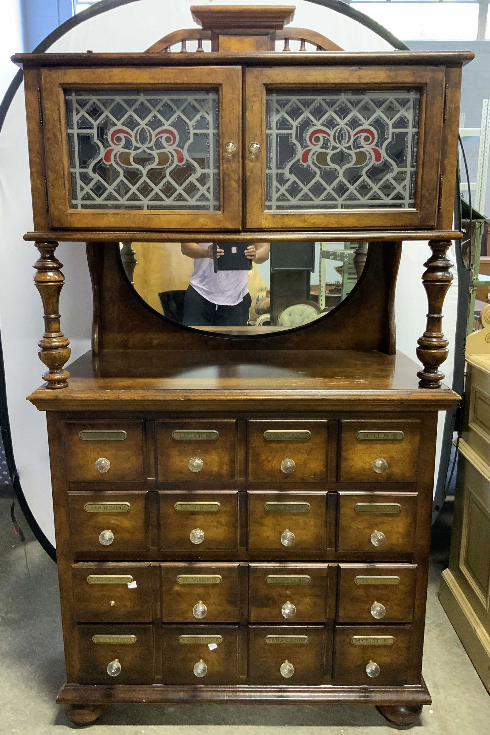 Pulaski Furniture Vtg Wooden Apothecary Cabinet: Backside of apothecary cabinet has tag which reads PULSAKI FURNITURE. Apothecary cabinet is vintage and wooden. Piece has stained glass door cabinet at top. Lower half has 4 drawers with gilt name pla