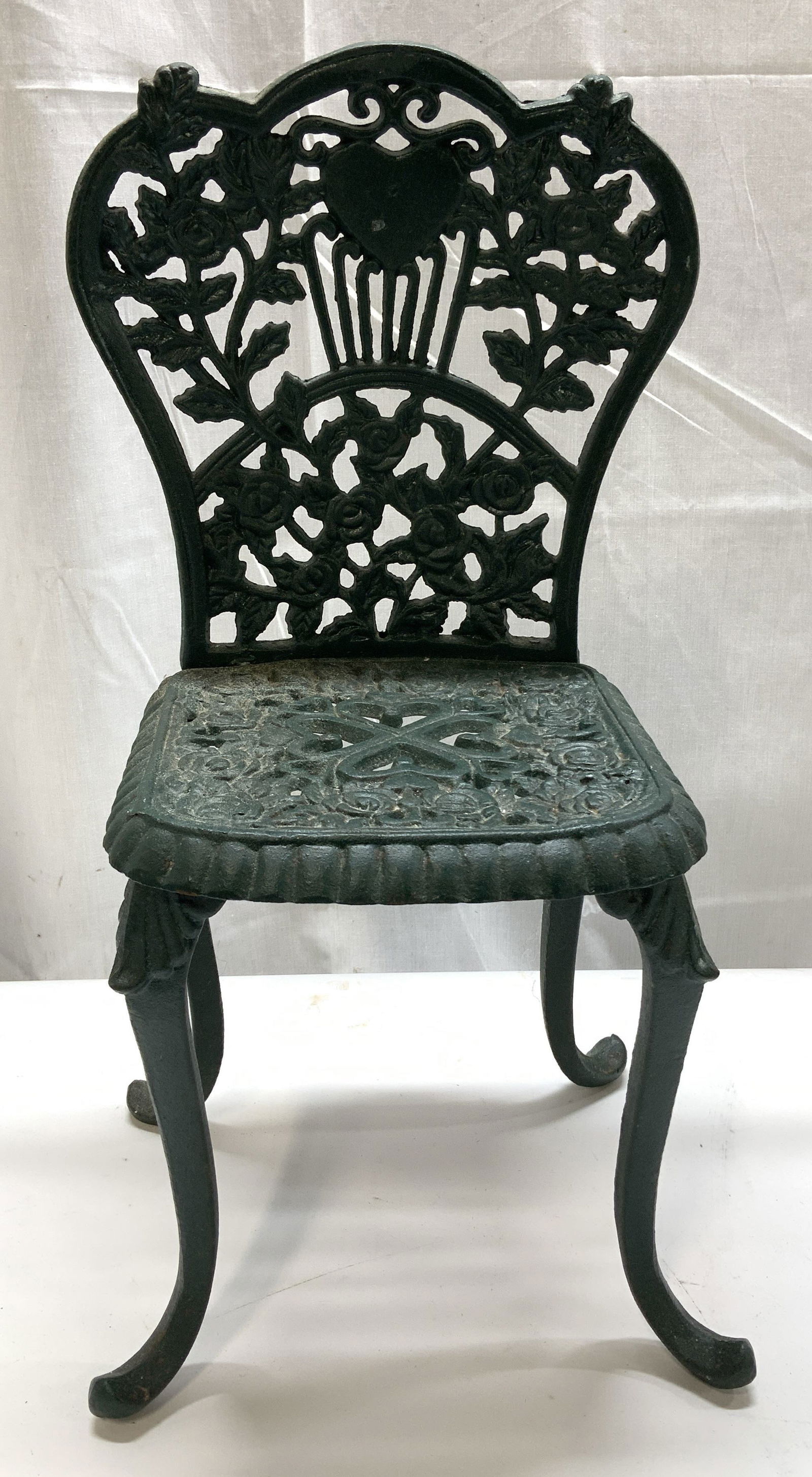Vintage Cast Iron Miniature Ornate Green Chair: Miniature chair is dark green toned & cast iron material. Chair has a detailed backrest featuring a heart design at the top, surrounded by a fan-like pattern of roses. Surface wear consistent to age,