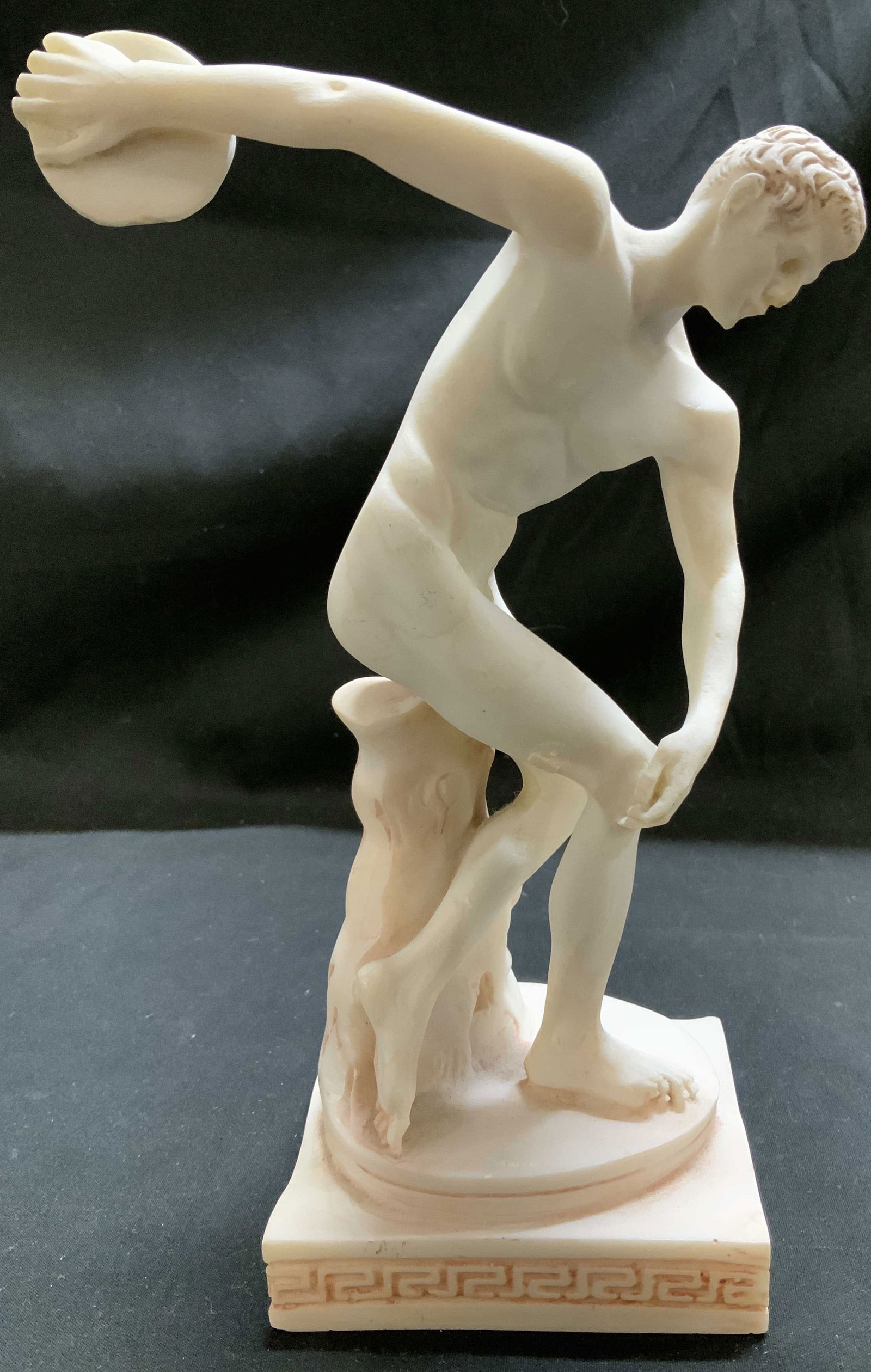 FESTOS Discobolus Greek Athlete Alabaster Fig: Figurine is genuine alabaster material. Depicts a young athlete in the act of throwing a discus. Figurine is hand-made. Signed & marked on underside. Reads, GENUINE ALABASTER. FESTOS. HANDMADE. Surfac
