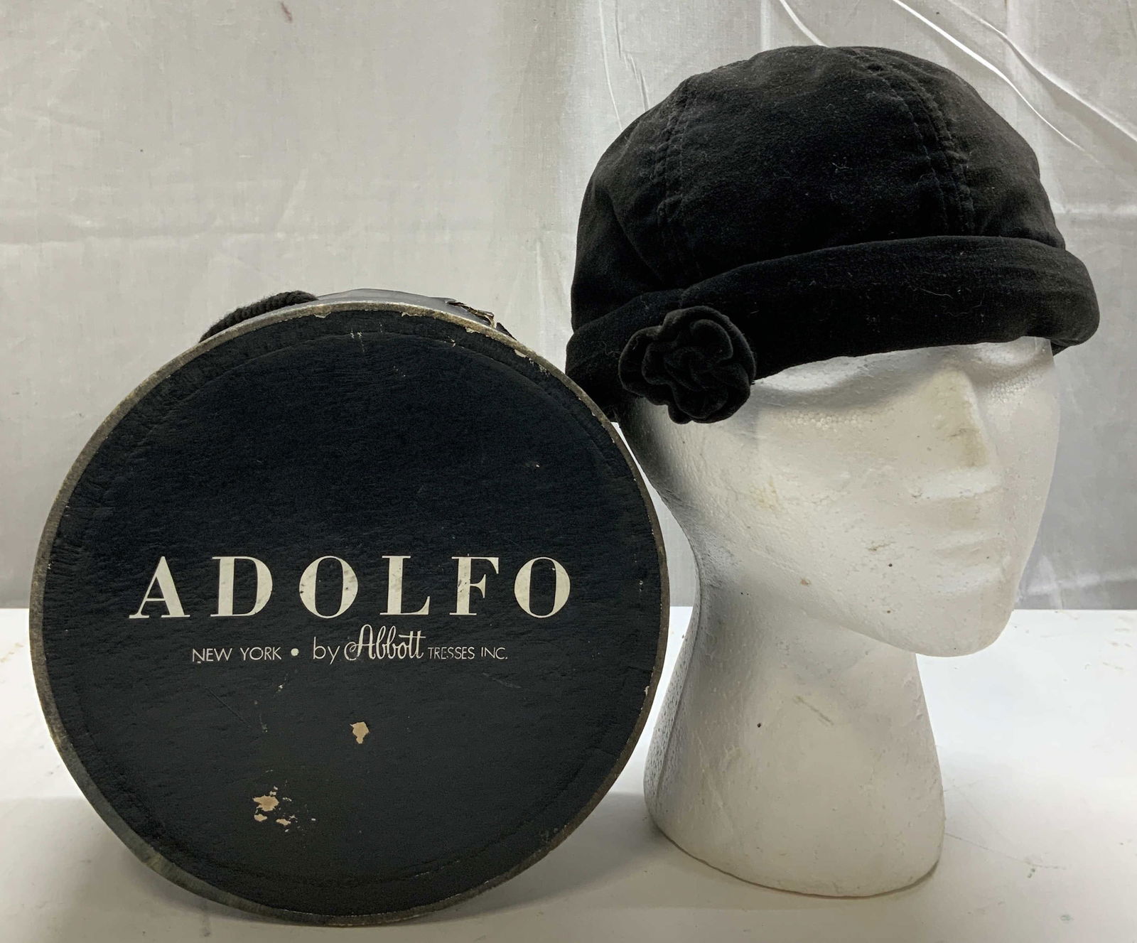 Vntg Adolfo Velvet Cloche Hat W Floral Accent: Vintage cloche-style hat appears to be made of black velvet or felt. Features a rounded crown & a rolled brim. Small flower accent is attached to rolled brim. Comes with box that reads, ADOLFO. NEW YO
