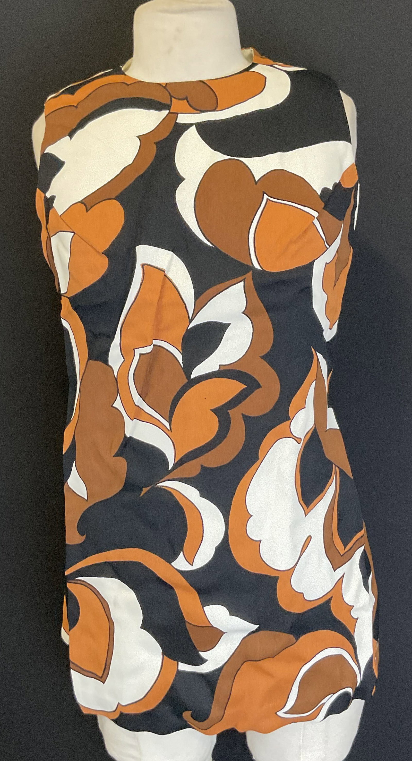 Vtg Brown Black Orange Synthetic Sleeveless Dress: Vintage brown black orange synthetic dress. Black, orange, white, brown floral patterned dress. Fully lined. Sleeveless, rounded neck. Back zipper. 17 inches across chest. Some discoloration observed.