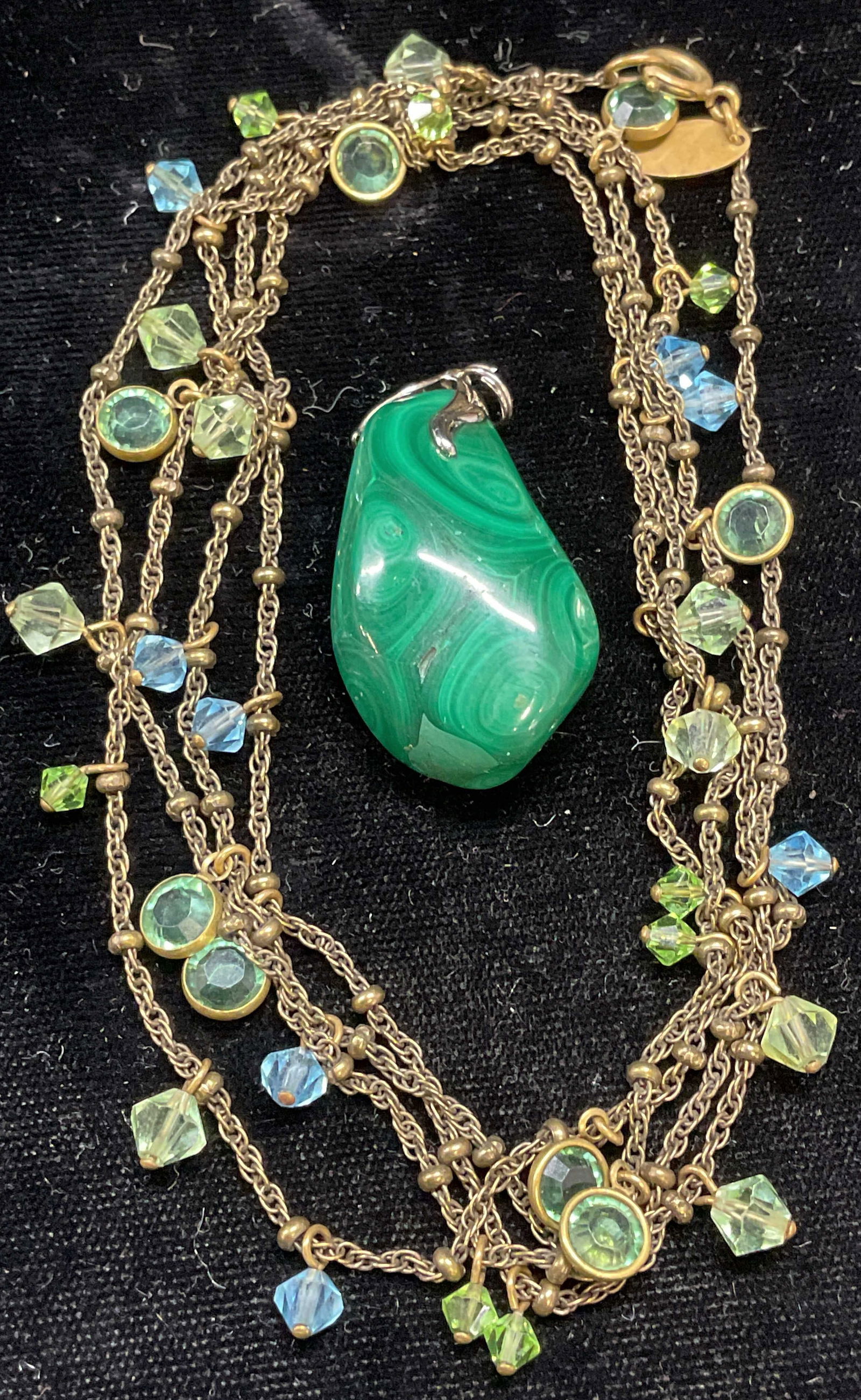 Lot 2 Lizpaiacios SF Crystal Necklace, Malachite: Lot of 2 jewelry pieces. Malachite pendant. Measures approx 1.5 x .75 inches. Lizpaiacios S. F. gold tone green and blue crystal necklace. Signed. Drop length approx 21 inches. Some scratching. Jewelr