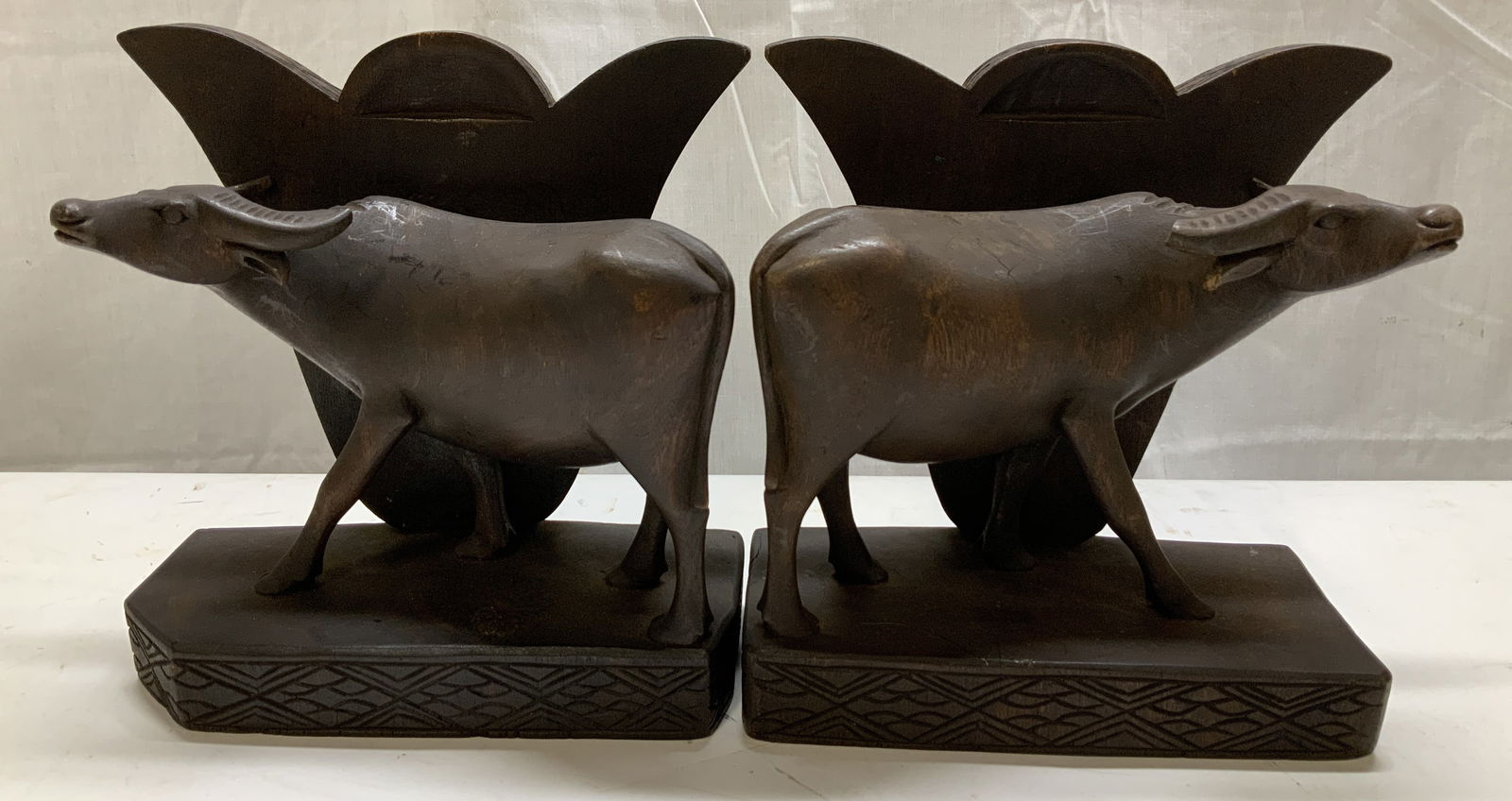Vntg Hand Carved Wooden Oxen Bookends: Bookends are hand-carved & wooden material. Depict oxens standing on a hand-carved base w a fan like shape behind it. Piece is dark-toned. Surface wear consistent to age, use & exposure. Visible chipp