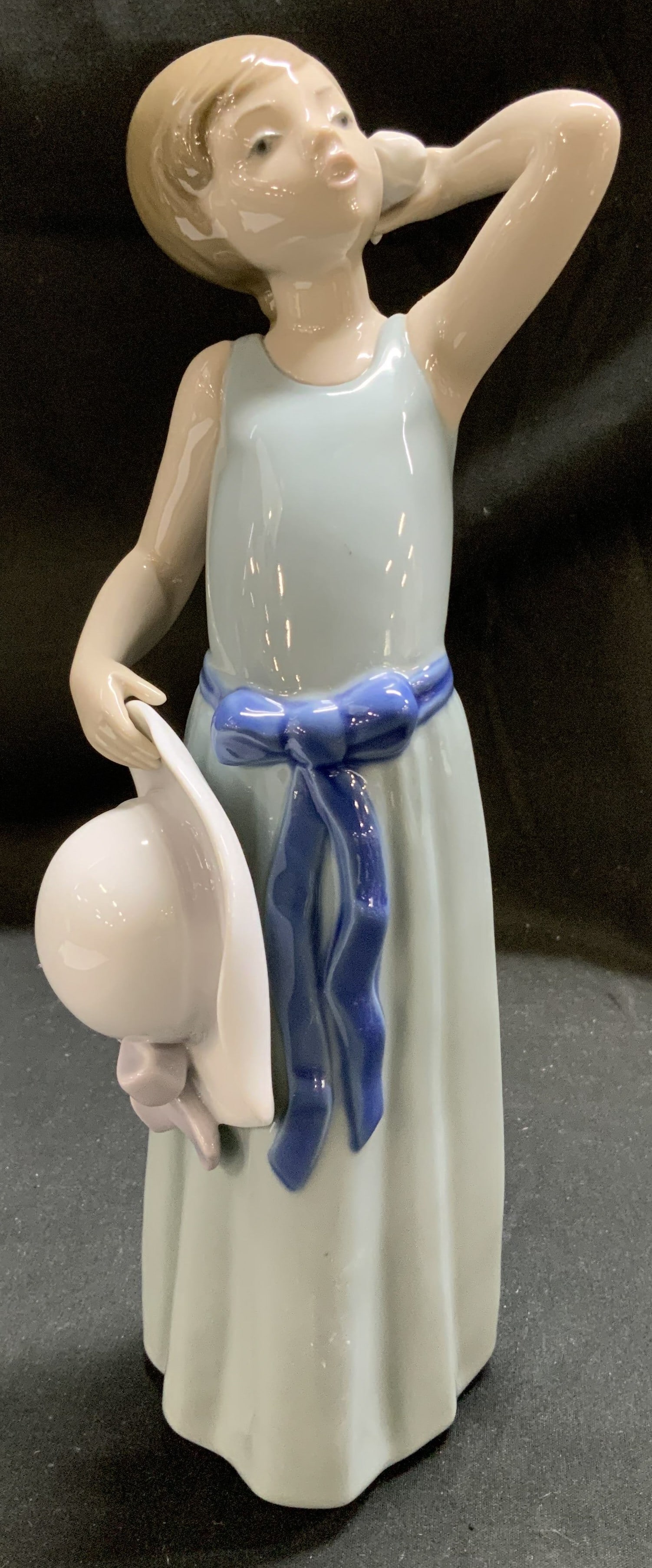 1978 LLADRO Prissy W Hat Porcelain Figurine SPAIN: Porcelain figurine is wearing a pale blue sleeveless dress with a blue sash tied in a bow around her waist. She holds a white hat in her left hand while her right hand is raised to her head. Signed &