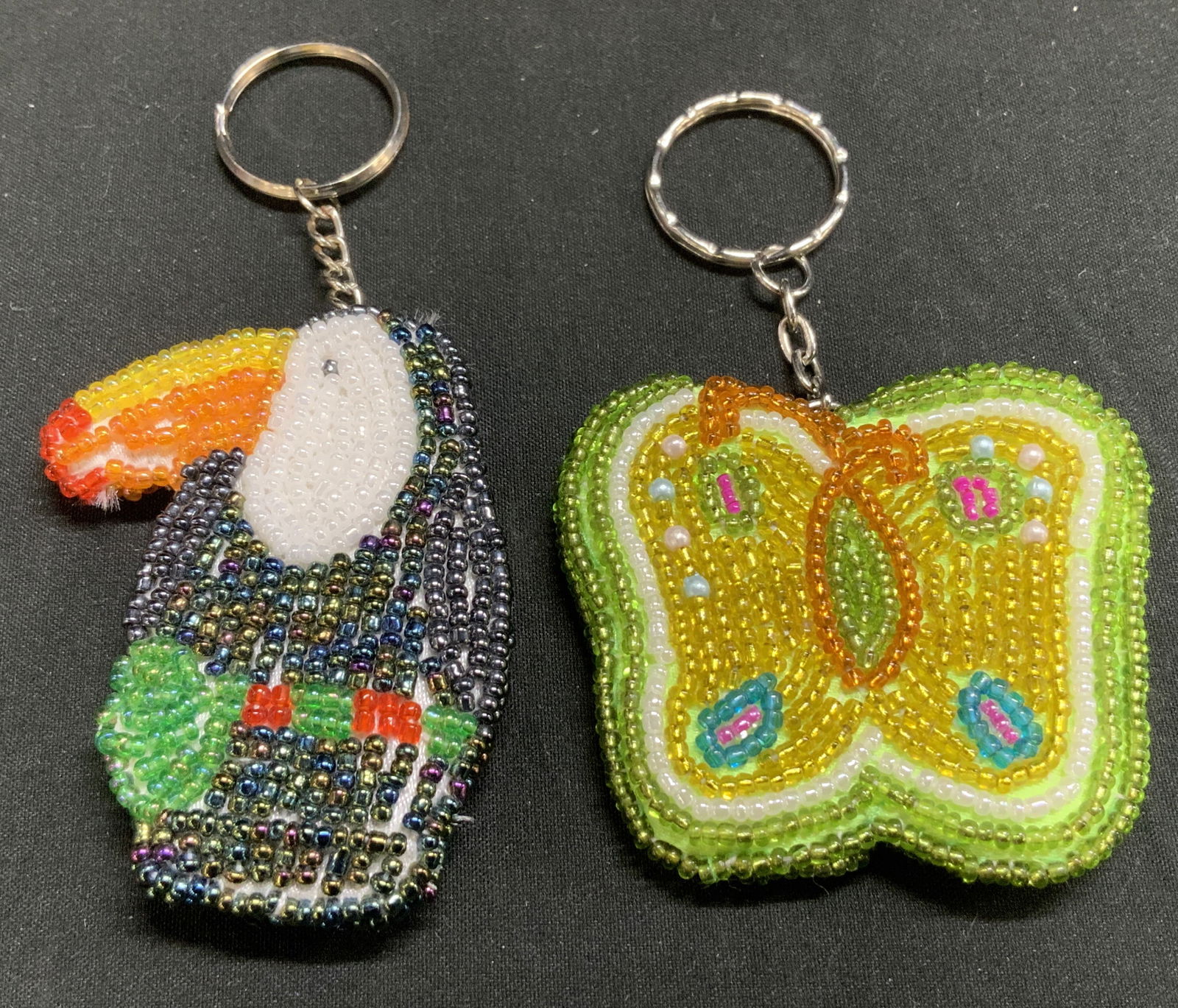Lot 2 Butterfly & Toucan Beaded Keychains: Lot includes, 2 beaded keychains, one shaped like a butterfly and the other like a toucan. Butterfly features yellow & green tones. Toucan features a colorful beak. Keychains appear to be hand-made. S