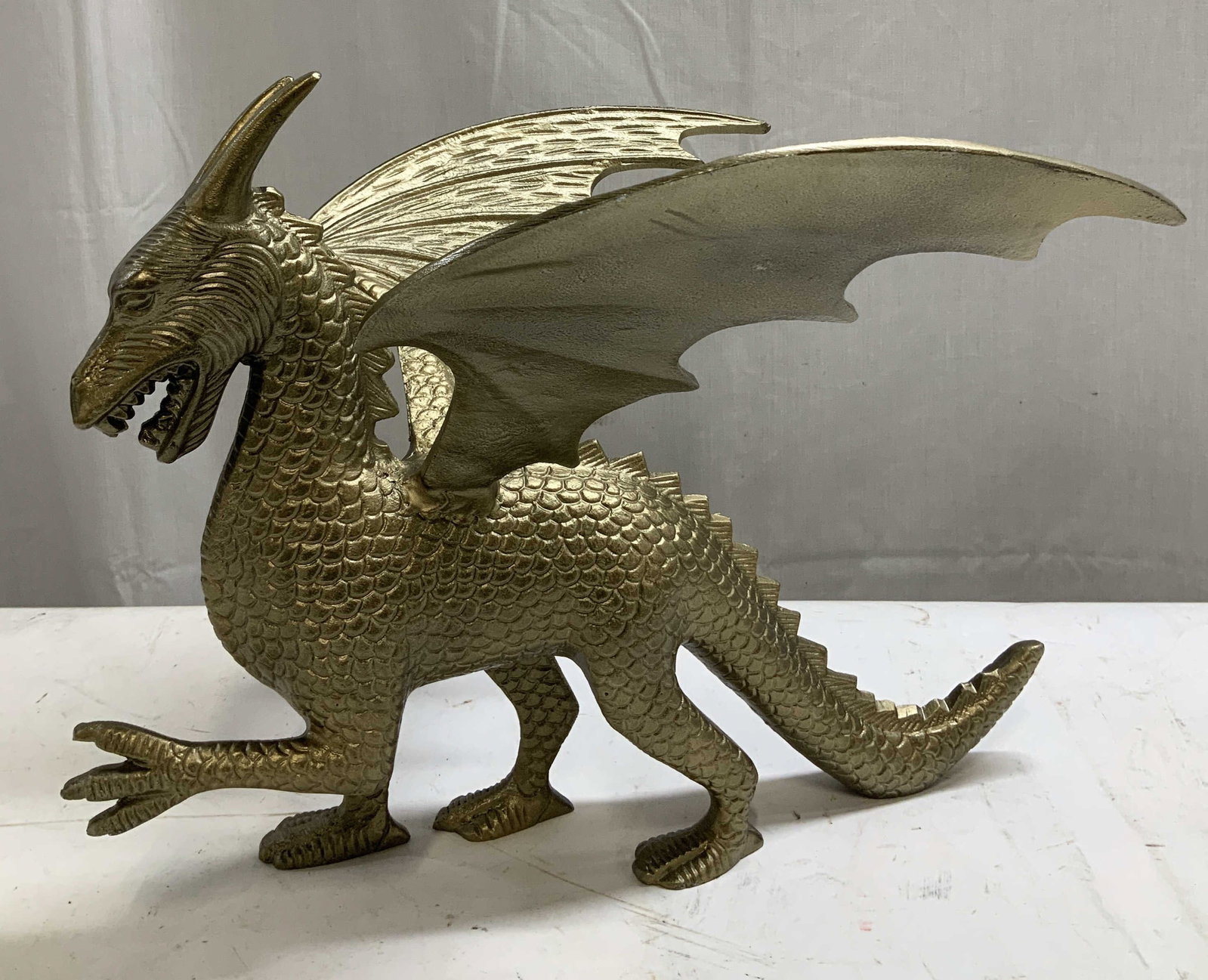 Large Golden Dragon Brass Tnd Metal Figurine: Piece appears to be white metal material with brass toned finish. Depicts a golden dragon figurine w large wing, & a single head with horns and an open mouth. No visible signature or markings. Surface