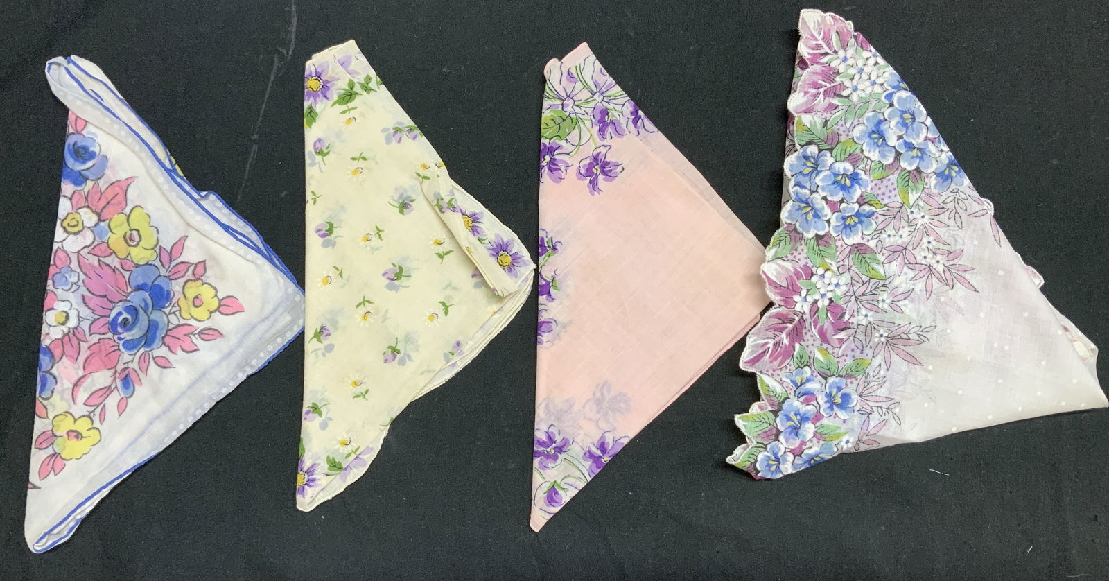 Lot 4 Vntg Assorted Floral Handkerchiefs: Handkerchiefs appear to be cotton material. Feature floral patterns in shades of yellow, blue, pink, & purple. 1 handkerchief has a scalloped edge. Surface wear consistent to age, use & exposure. Meas