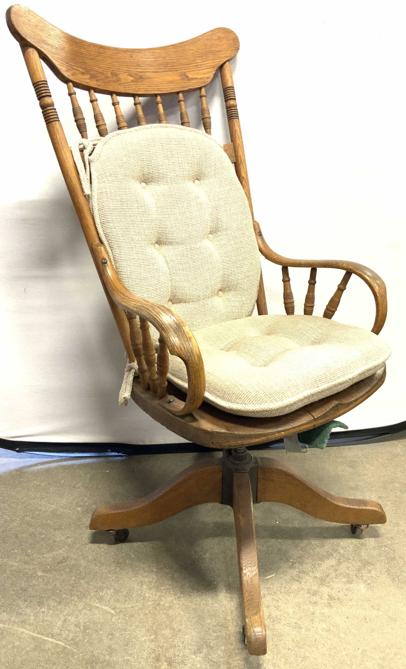 Vintage Wooden Office Chair On Casters: Office chair is vintage and wooden. piece is tan toned. Chair has carved spindle backrest. Office chair has armrests. Chair sits on 4 casters. Piece includes tan toned tufted cushions. Office chair me