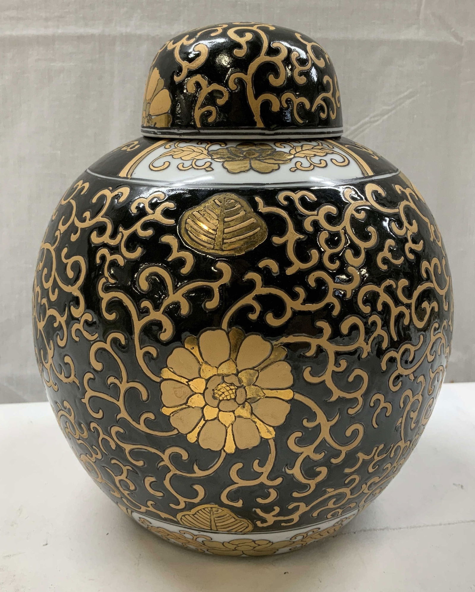 Vntg Black & Gold Floral Lidded Ginger Jar: Lidded porcelain jar featuring an intricate gilt floral & scrollwork design. Glossy finish. Surface wear consistent to age, use & exposure. Measurements: length 6.5in x width 6.5in x height 9in. Vinta