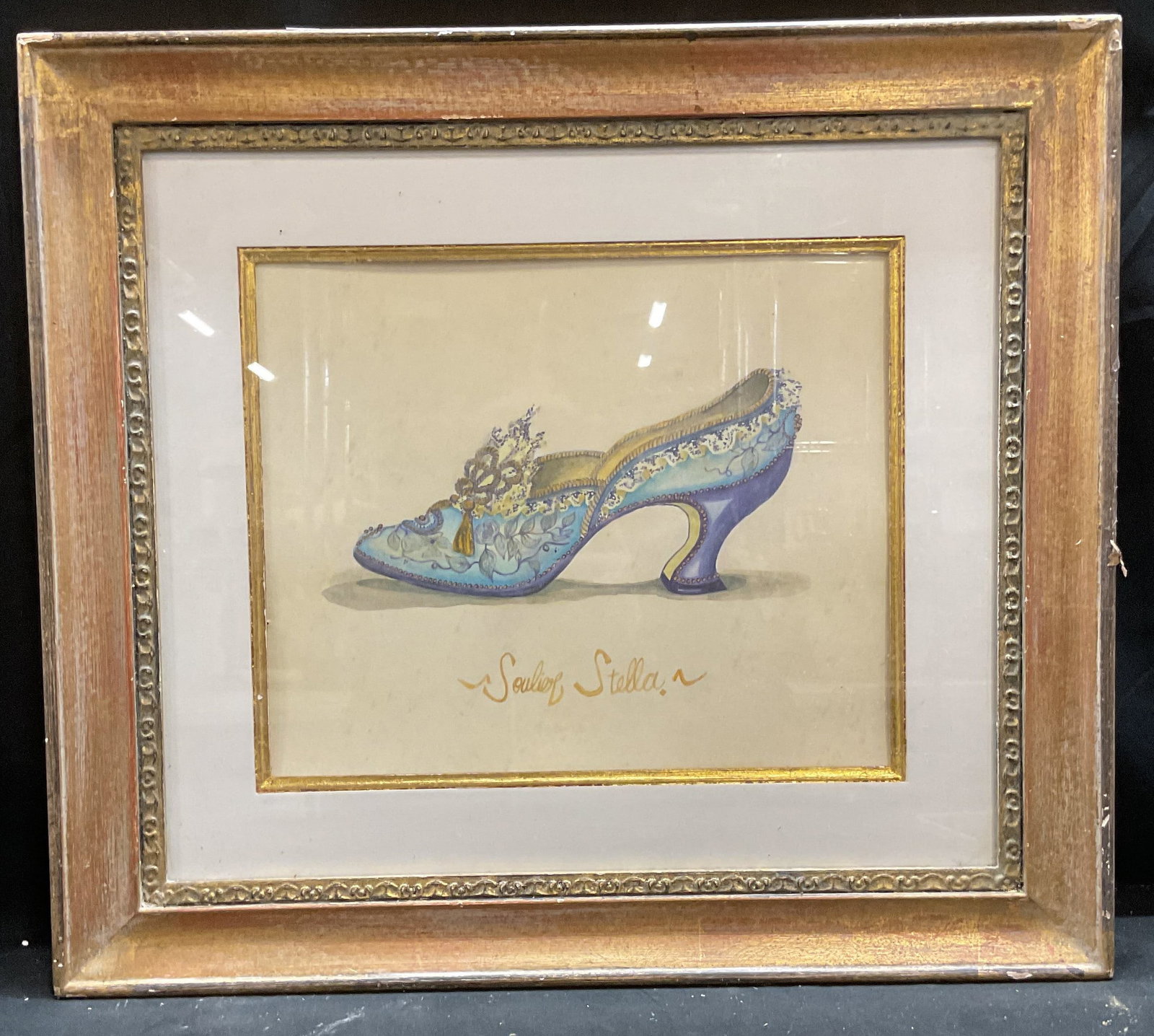 Framed Soulier Stella Victorian Shoe Litho: Framed and matted lithograph on paper. Soulier Stella, Victorian style blue heeled shoe. Decorative gilt wood frame. Not examined out of frame. Frame measures approx 19.5 x 22 inches. Some wear consis