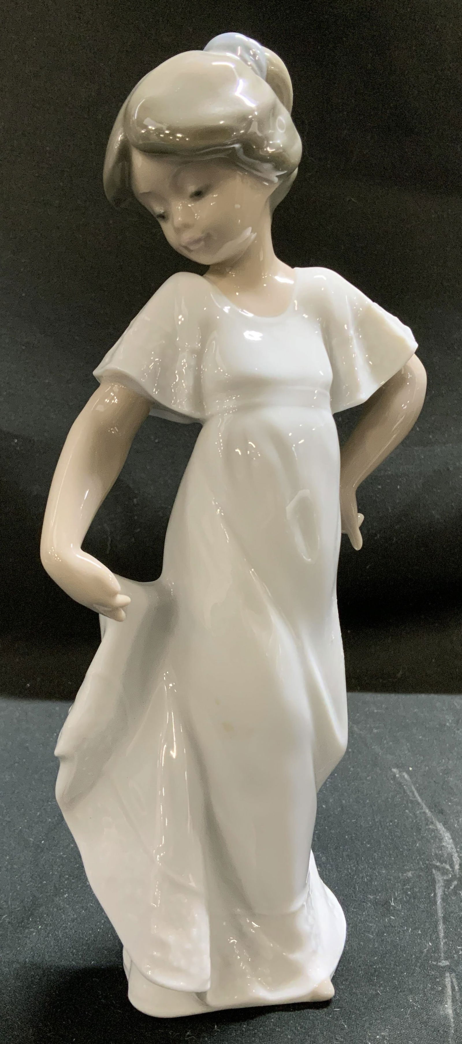 Nao Lladro How Pretty Porcelain Figural SPAIN 1989: Figurine depicts a young girl wearing a flowing white dress with ruffled cap sleeves. She is posed with one hand on her hip & the other holding the hem of her dress. Signed & marked on underside. Read