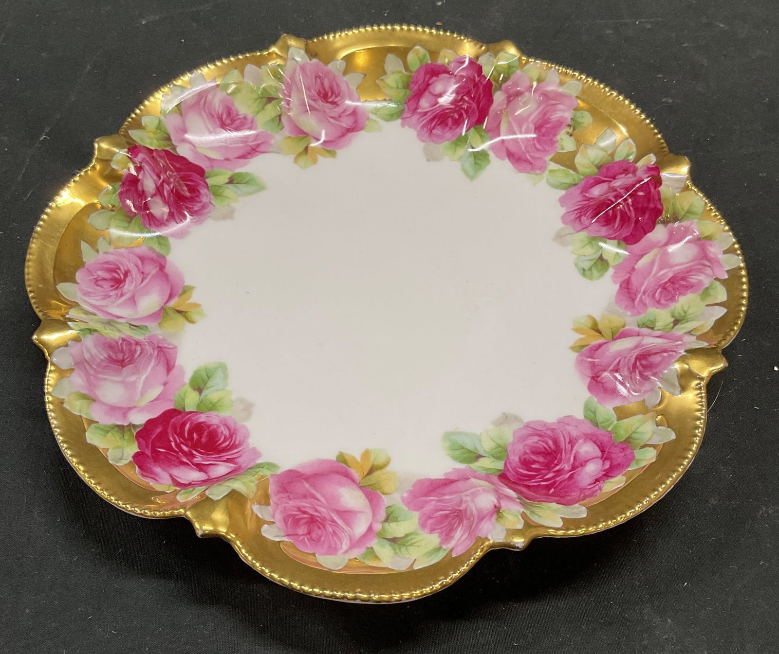 Antique Sgn Gilt Porcelain Floral Plate, Austria: Antique porcelain plate. Crown and crossed hammer backstamp on underside. Made in Austria. Hand painted decoration, pink floral and gilt border. Scalloped rim. Measures approx 8.5 inches wide. Some sc