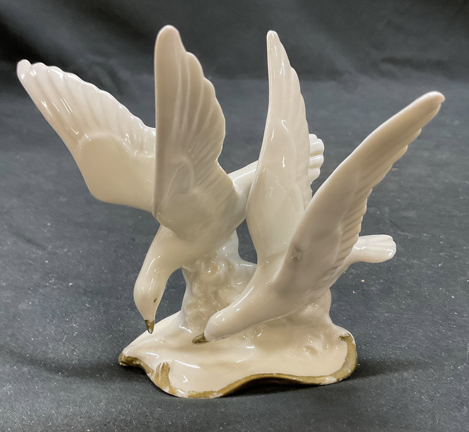 Vtg White Porcelain Seagulls in Flight Figurine: Vintage white porcelain seagulls in flight figurine. 2 seagulls with spread wings. Gold rim and beak detail designs. 5 x 4 x 4.25 inches. Some surface wear consistent with exposure. Seagulls in flight