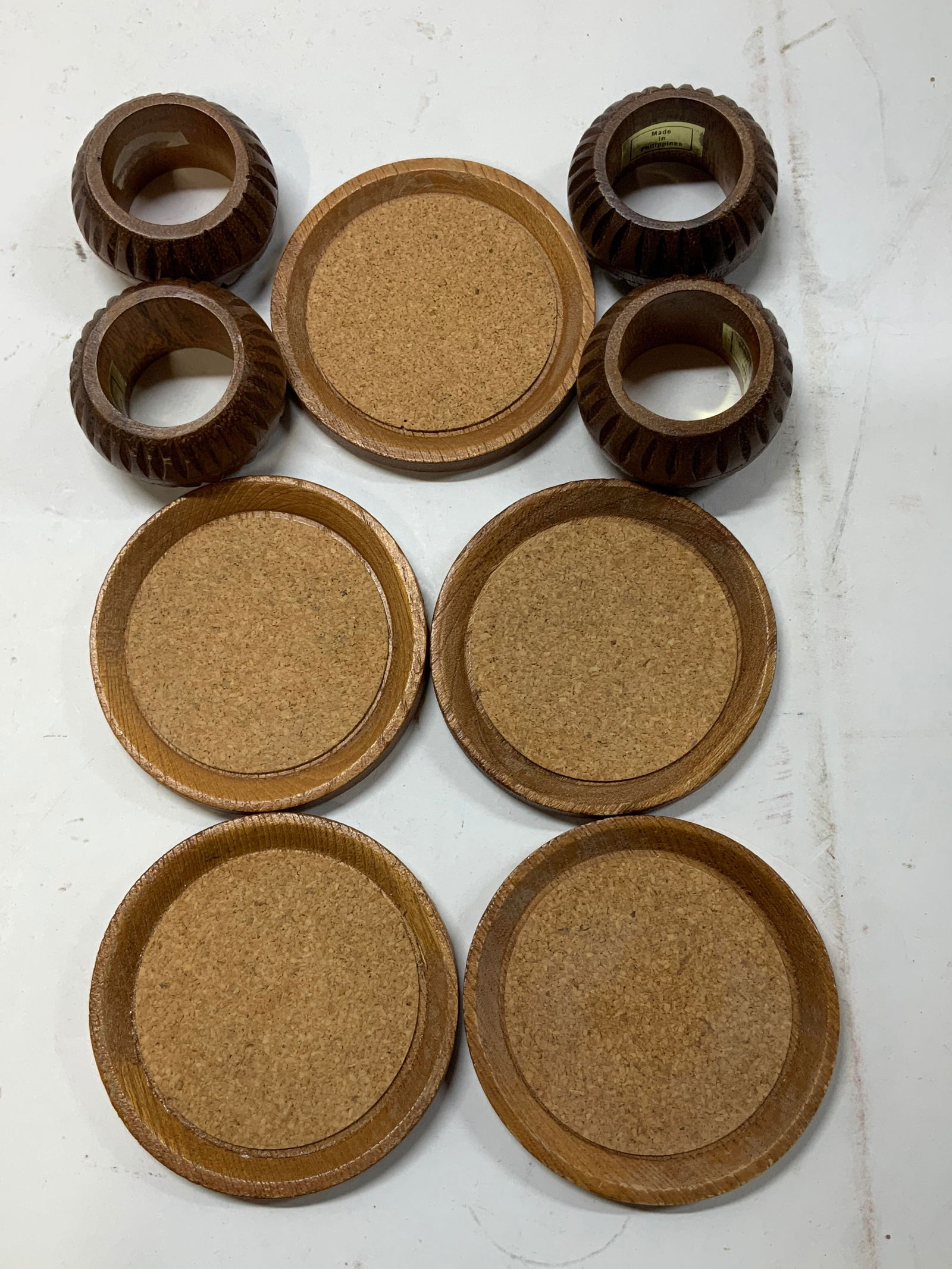 Lot 9 Wooden Coasters & Carved Napkin Rings: Lot includes, 5 wooden coaster with a cork insert & 4 wooden carved napkin rings. Signed & marked on napkin rings. Reads, MADE IN PHILIPPINES. Surface wear consistent to age, use & exposure. Measureme