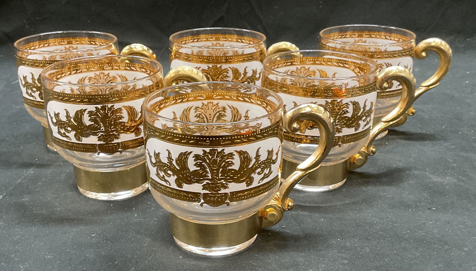 Set 6 Gilt Glass Ornate Scroll Cups: Set of 6 cups with handles. Glass and metal. Gilt with white. Ornate scroll design. Measure approx 3 x 3.5 inches. Some scratching and loss to paint. Gilt cup, glass cup, ornate cup, tableware, table