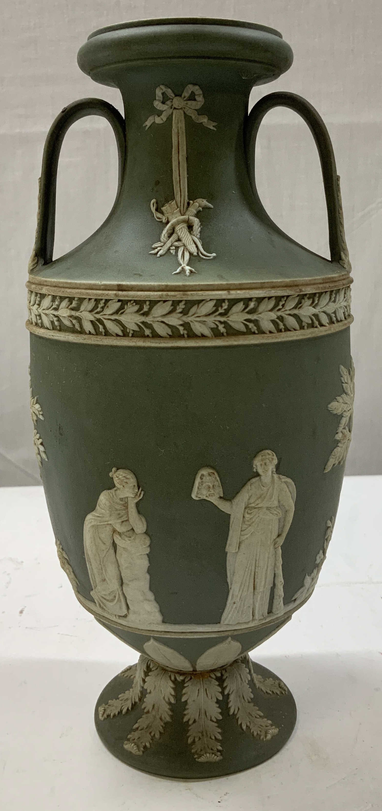 Wedgwood Green Jasperware Trophy Vase ENG: Wedgwood green jasperware pedestal trophy vase. Body of vase is adorned with white neoclassical reliefs surrounded by a raised foliate border. Surface wear consistent to age, use & exposure. Signed &