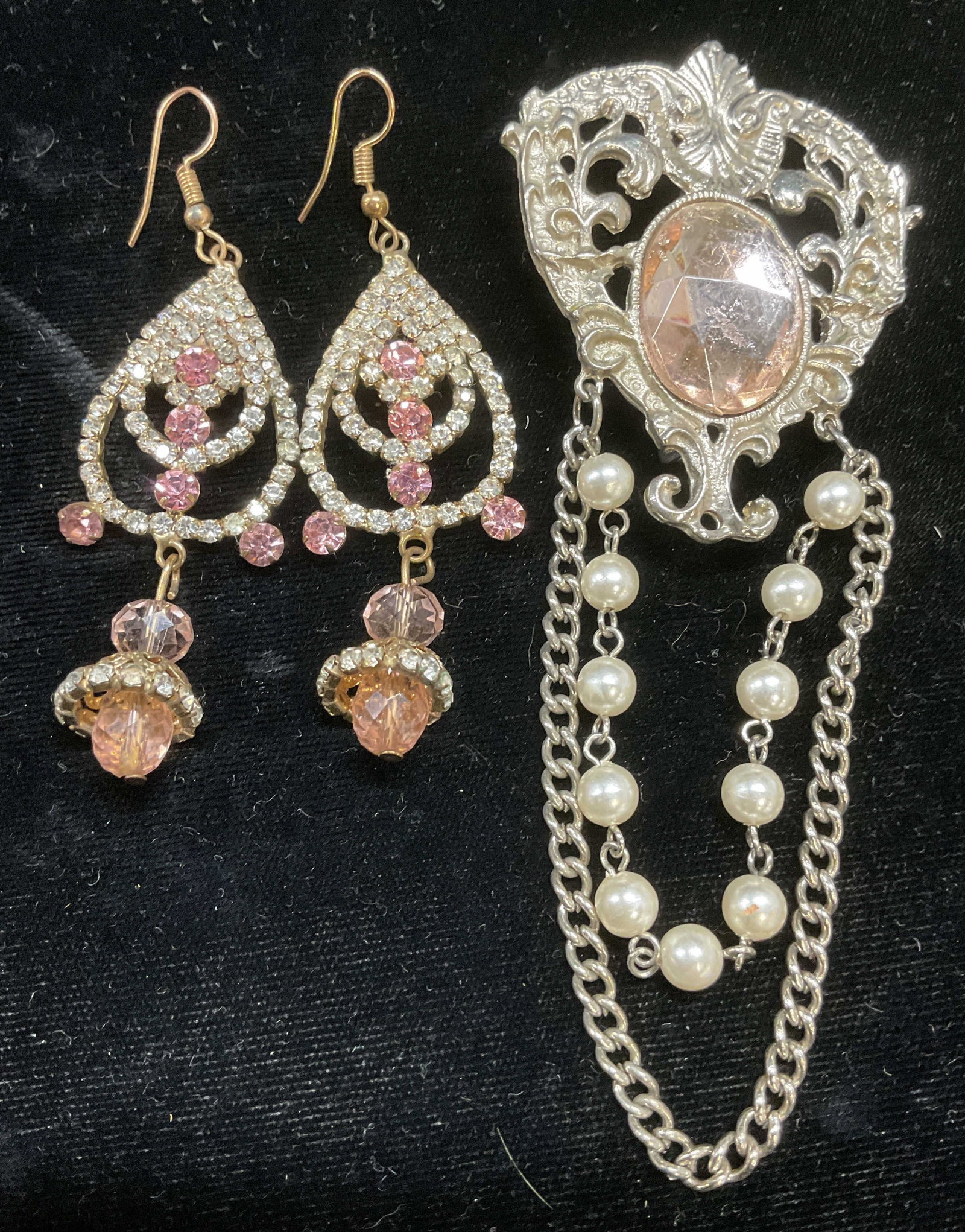 Lot 2 Pink Crystal Brooch & Earrings, 4.75 In L: Lot of 2 jewelry pieces. Gold tone pink and colorless crystal dangle earrings. Measure approx 2.5 inches long. Silver tone scroll motif brooch with dangling chain and faux pearls, and central pink cry