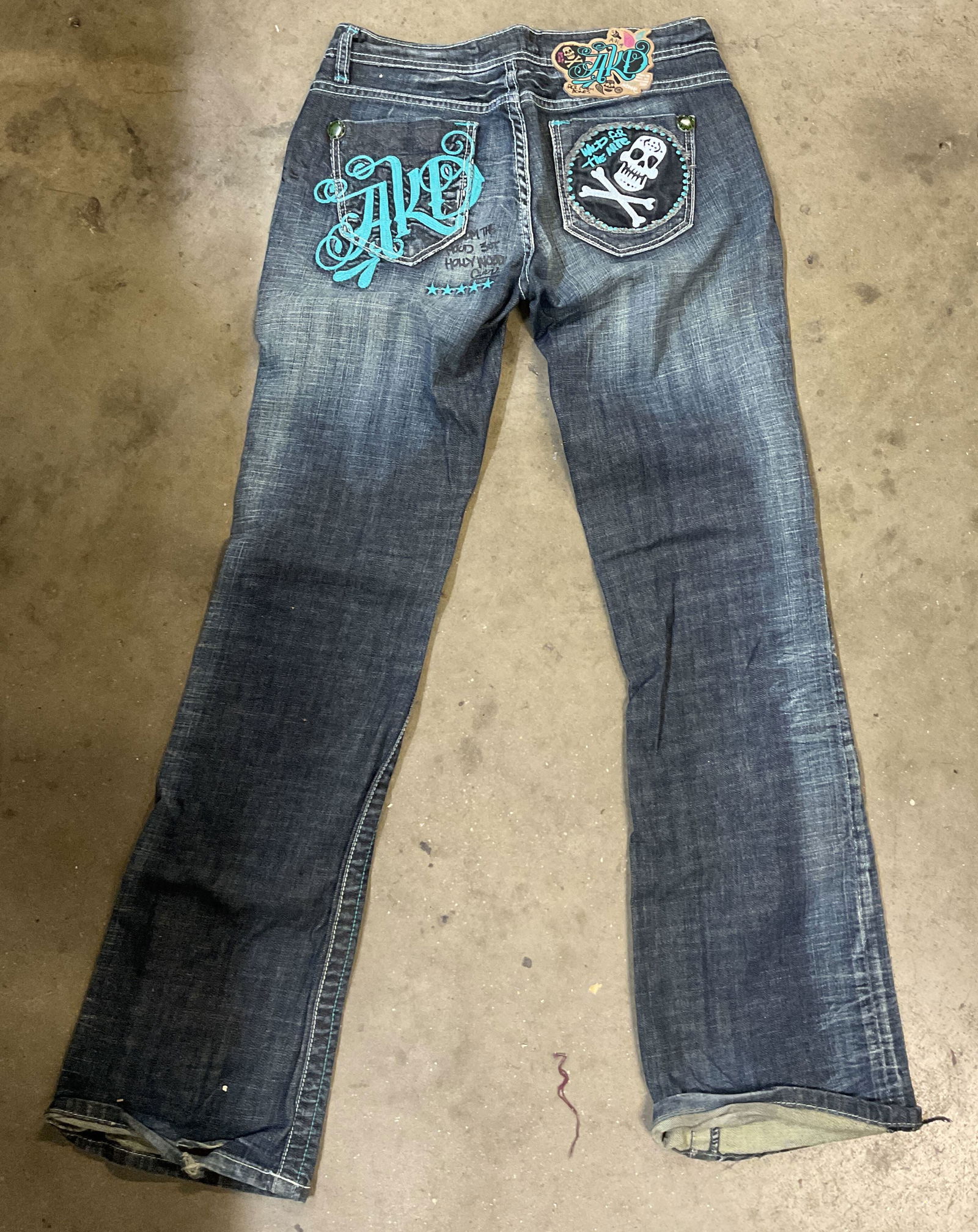 Akademiks Embroidered Jeans: Akademiks embroidered jeans. Size 28. Skull patch and graffiti graphic on back pockets. Silver toned pendant on front belt loop. Patch on waist. Cotton material. Dark blue wash. Embroidery on front. M