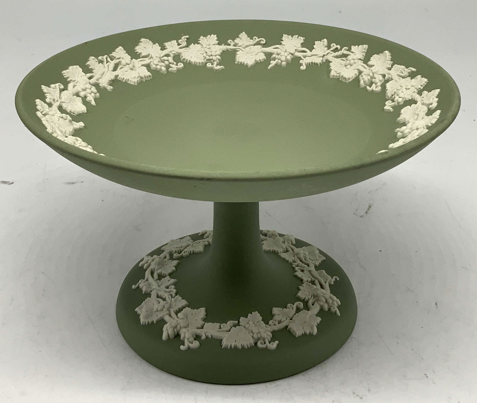 Wedgwood Green Jasperware Pedestal Dish ENGLAND: Pedestal dish has a green matte body w raised white grapevine motifs. Grapevine motifs on base & rim. Surface wear consistent to age, use & exposure. Signed & marked on underside. Reads, WEDGWOOD MADE