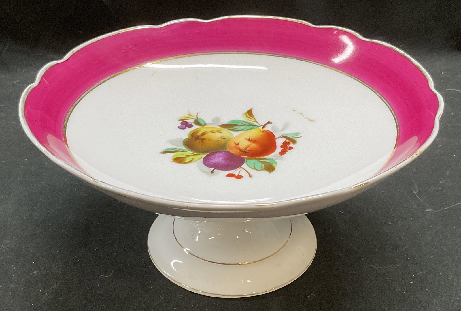 Signed CT Porcelain Fruit Pedestal Bowl: Vintage signed porcelain pedestal bowl. Hand painted fruit motif center with gilt and magenta border. Scalloped rim. Signed, partially legible, backstamp and C. T. Measures approx 8.75 x 4.5 inches. S