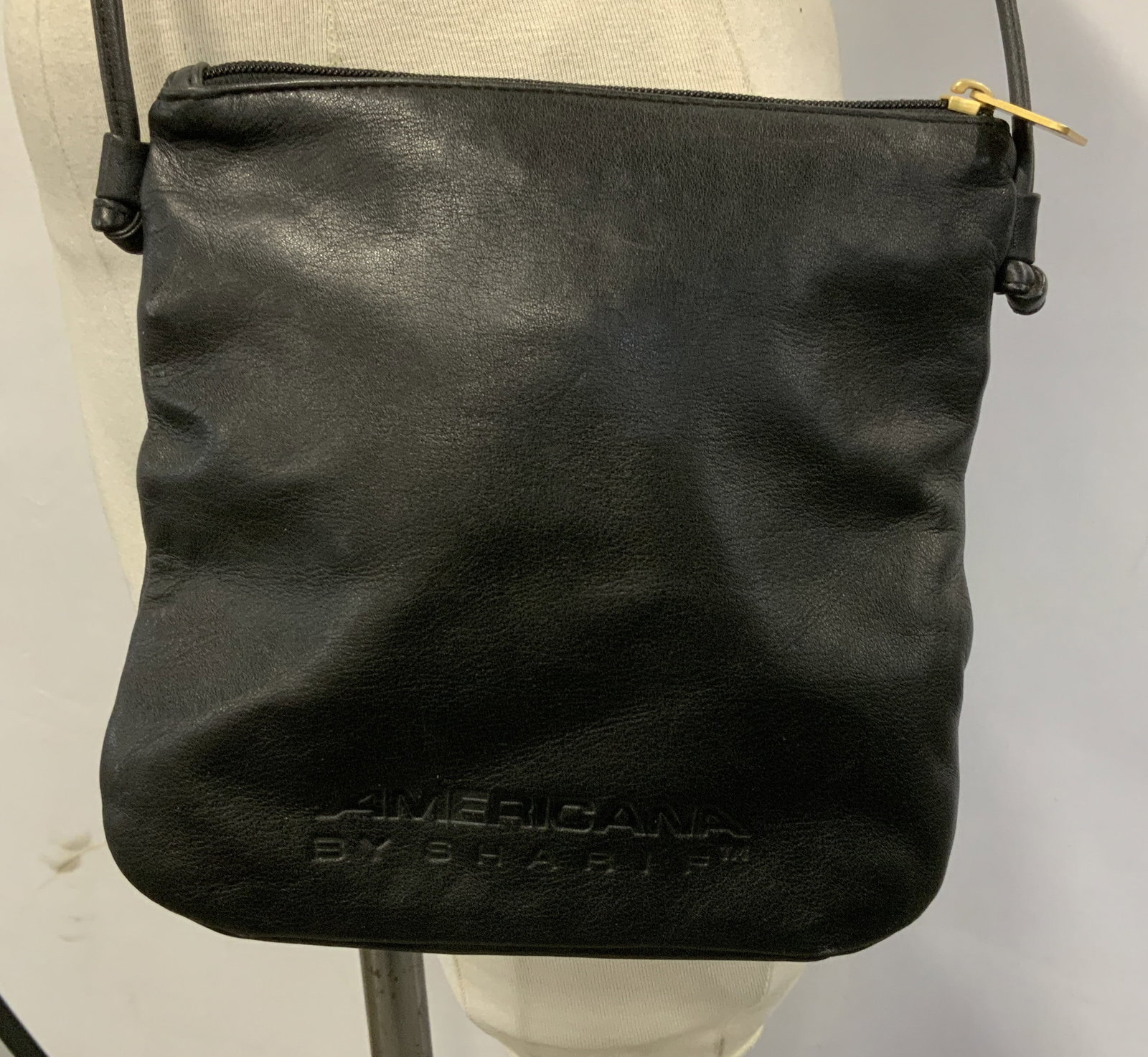 Americana by Sharif Black Leather Shoulder Bag: Shoulder bag has a zipper closure with gold-tone hardware. Front of bag has embossed lettering that reads, AMERICANA BY SHARIF. Signed & marked. Reads, AMERICANA BY SHARIF. Surface wear consistent to 