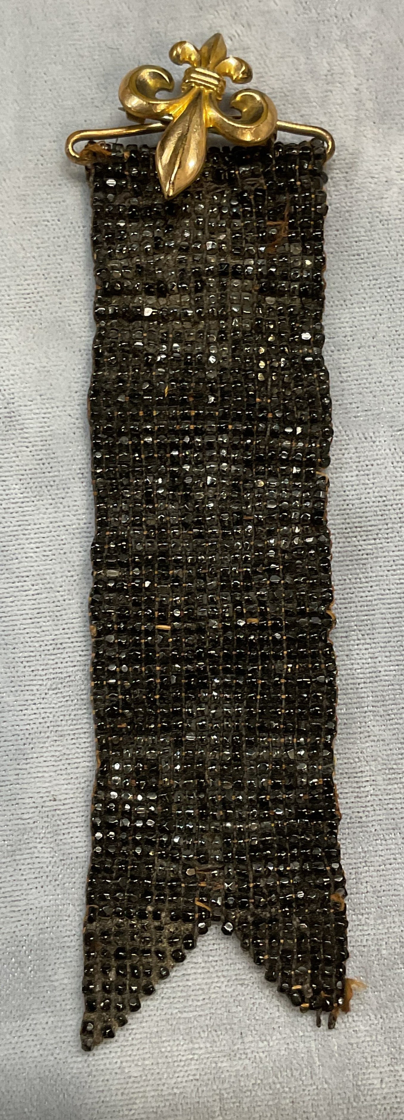 Sgn Gold Tn Fleur de Lis Brooch & Beaded Ribbon: Gold tone fleur de lis pendant brooch with black beaded ribbon. Signed illegibly. Measures approx 5 inches long. Some loss to beading. Some scratching. Jewelry, estate jewelry, costume jewelry, cockta