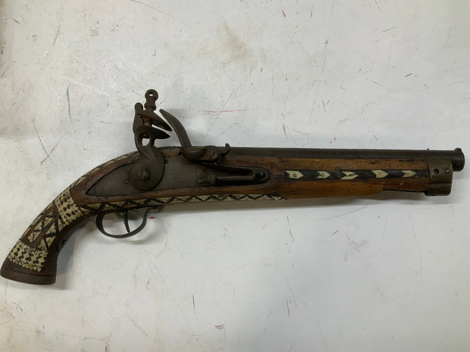 Antique Wooden & Bone Inlay Flintlock Pistol: Wood stocked flintlock style pistol featuring hand cut bone inlay in repeating geometric motifs. Metal lock mechanism. No visible signature or markings. Surface wear consistent to age, use & exposure.