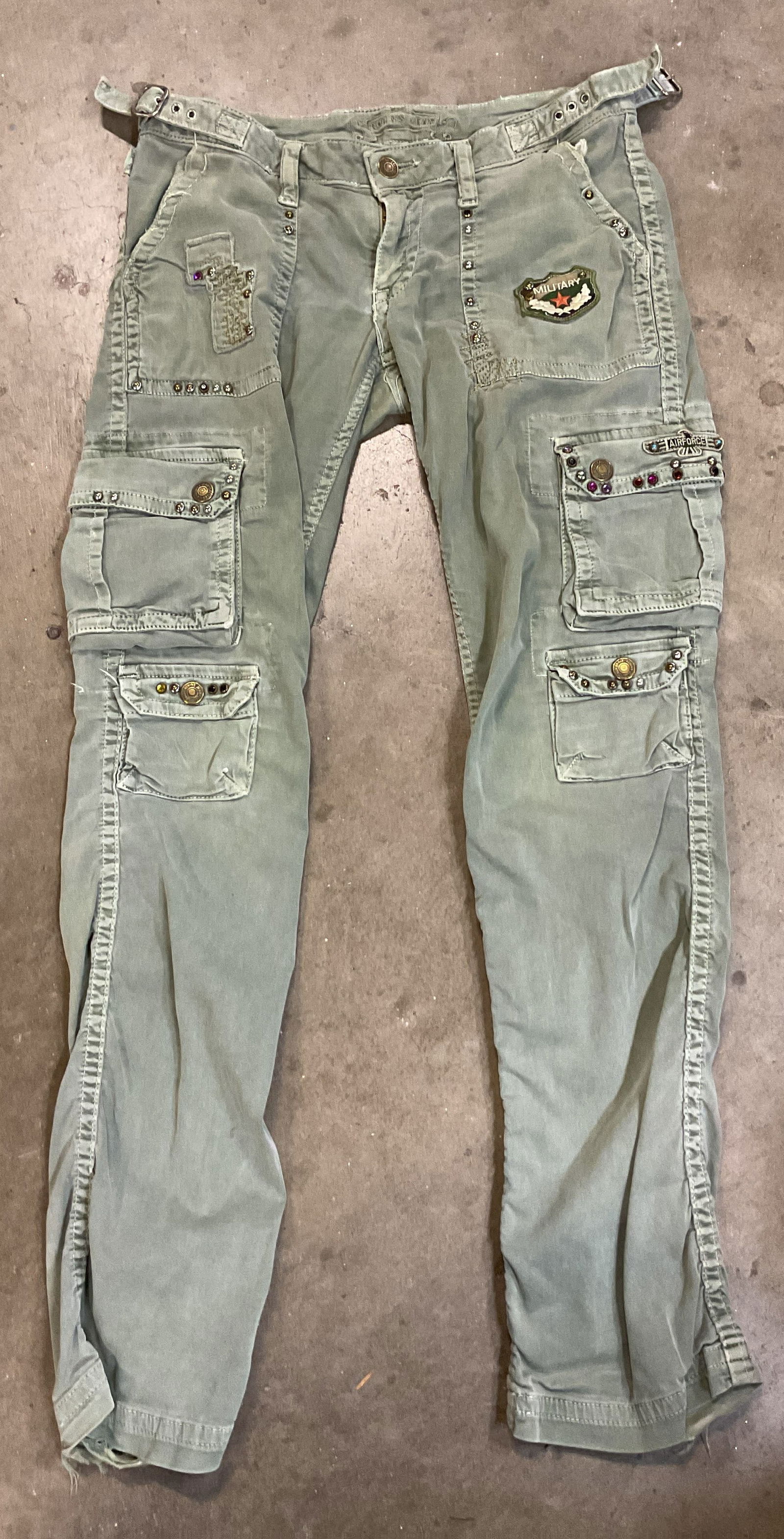 Robins Jean Green Embroidered Cargo Pants USA: Robins Jean army green embroidered and studded cargo pants. Size 27. Made in USA. Cotton material. Patch on front features a badge design that reads Military with gold toned studs. Another patch featu