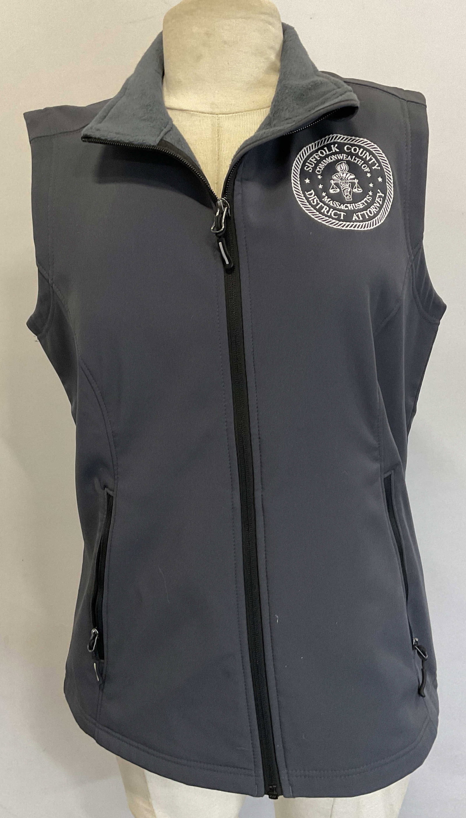Core 365 Grey Collared Graphic Vest: Core 365 grey collared graphic zip vest. Size M. Polyester material. Circular rope designed graphic that reads as follows Suffolk County Commonwealth Of Massachusetts District Attorney. Features colla