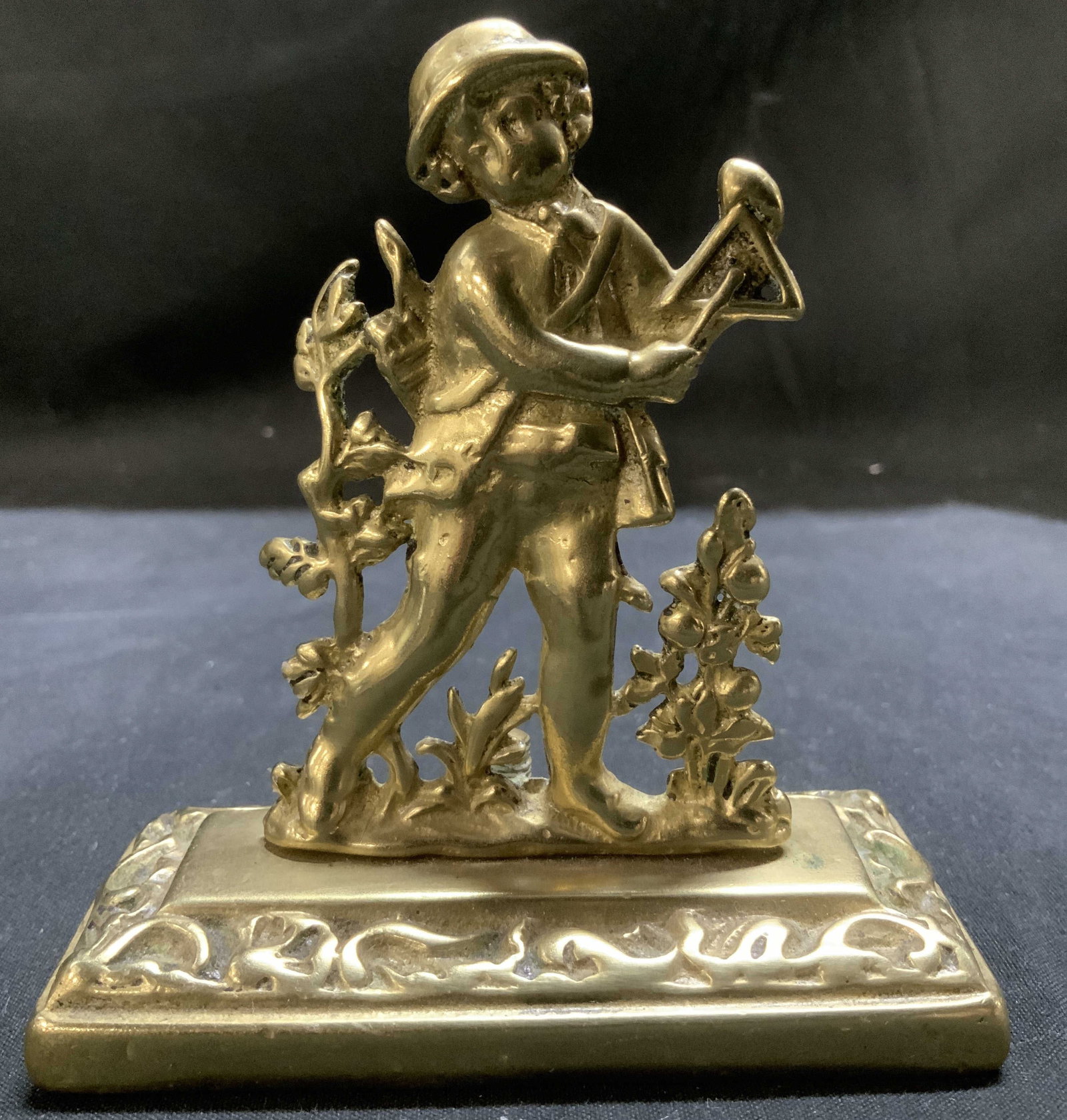 Vntg Brass Musician Boy Figurine: Figurine is brass & depicts a young boy in 18th century attire, holding a triangle instrument. Boy is surrounded by floral motifs. Rectangular base. Surface wear consistent to age, use & exposure. Mea