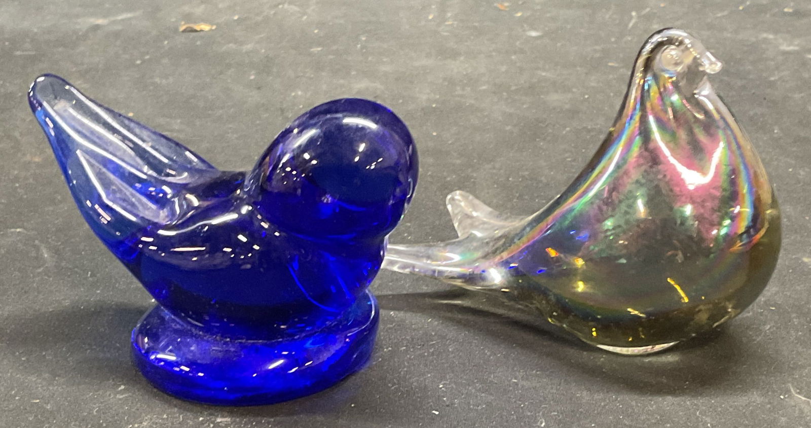 2 Cobalt & Iridescent Art Glass Bird Figurines: Lot of 2 hand blown art glass bird motif figurines or paperweights. Iridescent silver and cobalt blue. Larger piece measures approx 4 x 2.25 x 2.75 inches. Some scratching. Art glass bird, art glass p