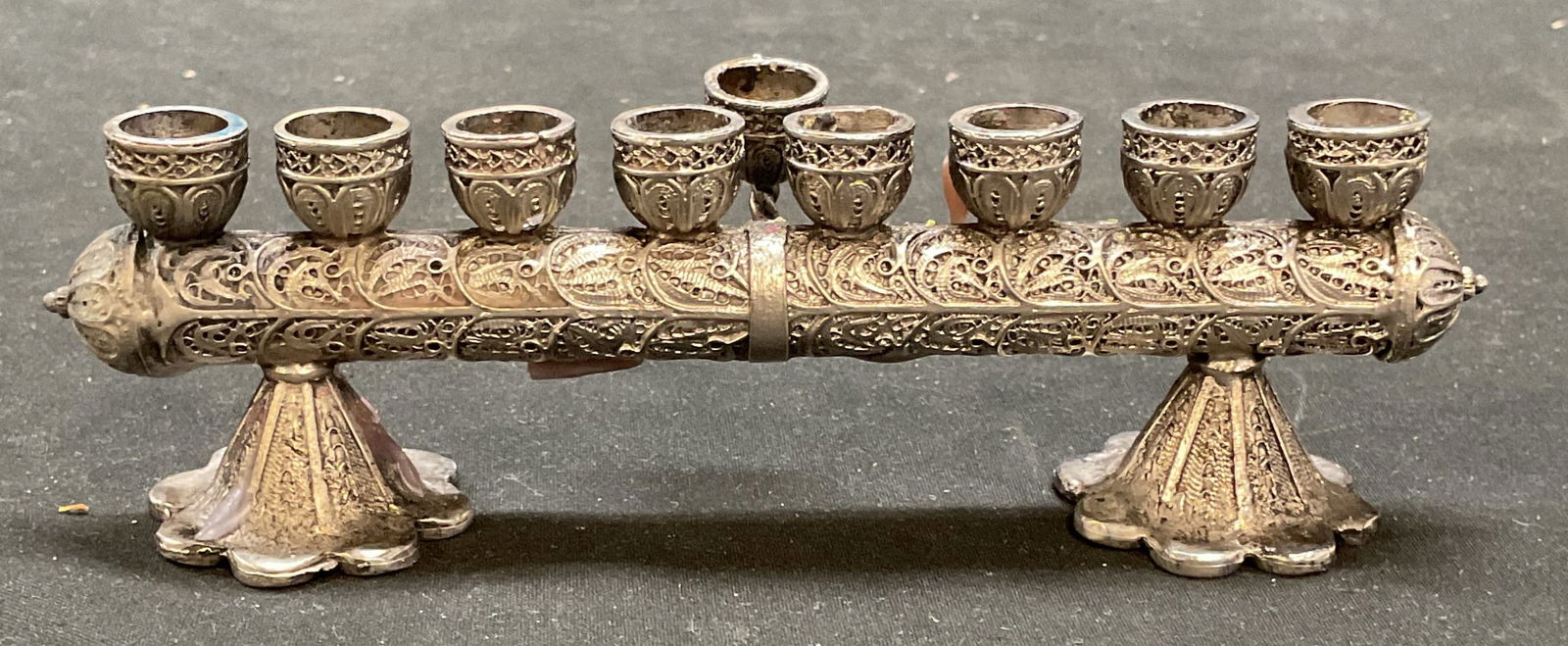 Silver Tn Filigree Menorah Shabbat Candle Holder: Silver tone ornate filigree menorah. Turn over for use as a Shabbat candle holder. Measures approx 6 x 1.5 x 1.75 inches. Some wear including scratching. Menorah, silver tone menorah, ornate menorah,
