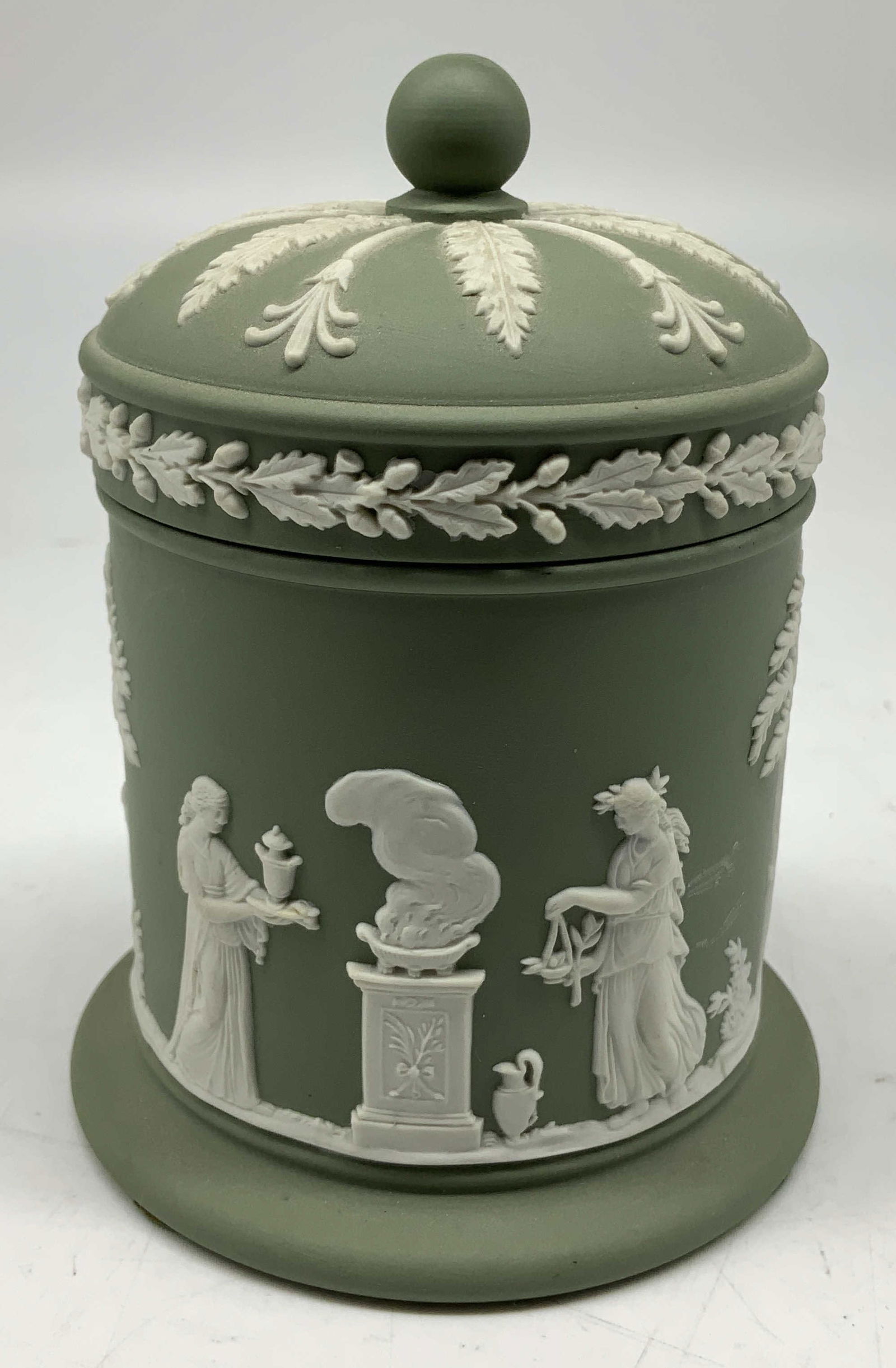 Wedgwood Green Jasperware Tobacco Jar ENGLAND: Tobacco jar comes w lid & features a decorative finial & acanthus leaf borders. Jars body features white relief Greek mythological & cupid figures. Signed & marked. Reads, MADE IN ENGLAND. WEDGWOOD. S