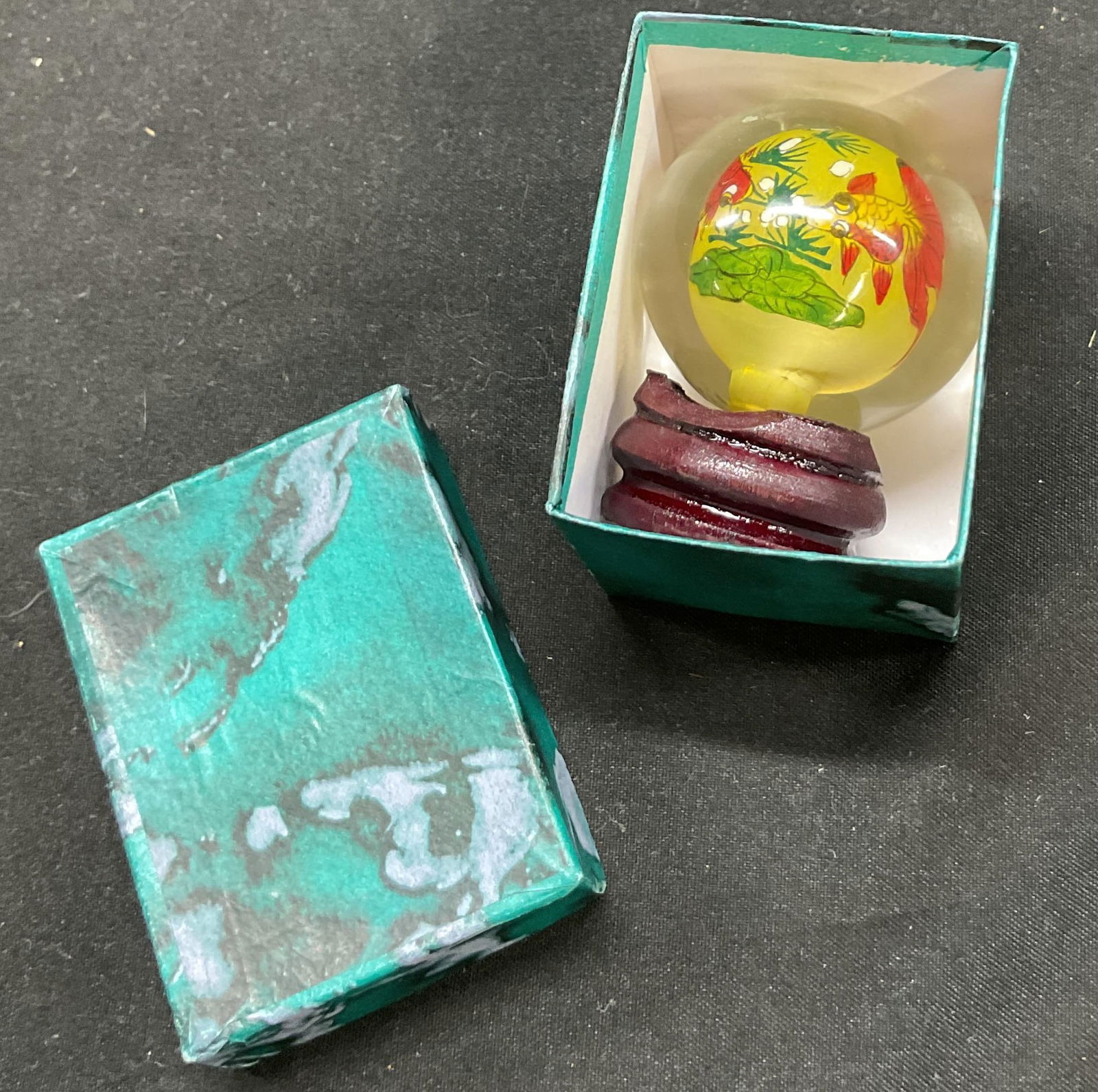 Art Glass Fish Sphere W Wood Stand & Box: Art glass fish design sphere. Comes with little wood stand and box. Clear sphere with another sphere inside. Features fish pattern in yellow, red, green, and white. Measures approx 3 inches in diamete