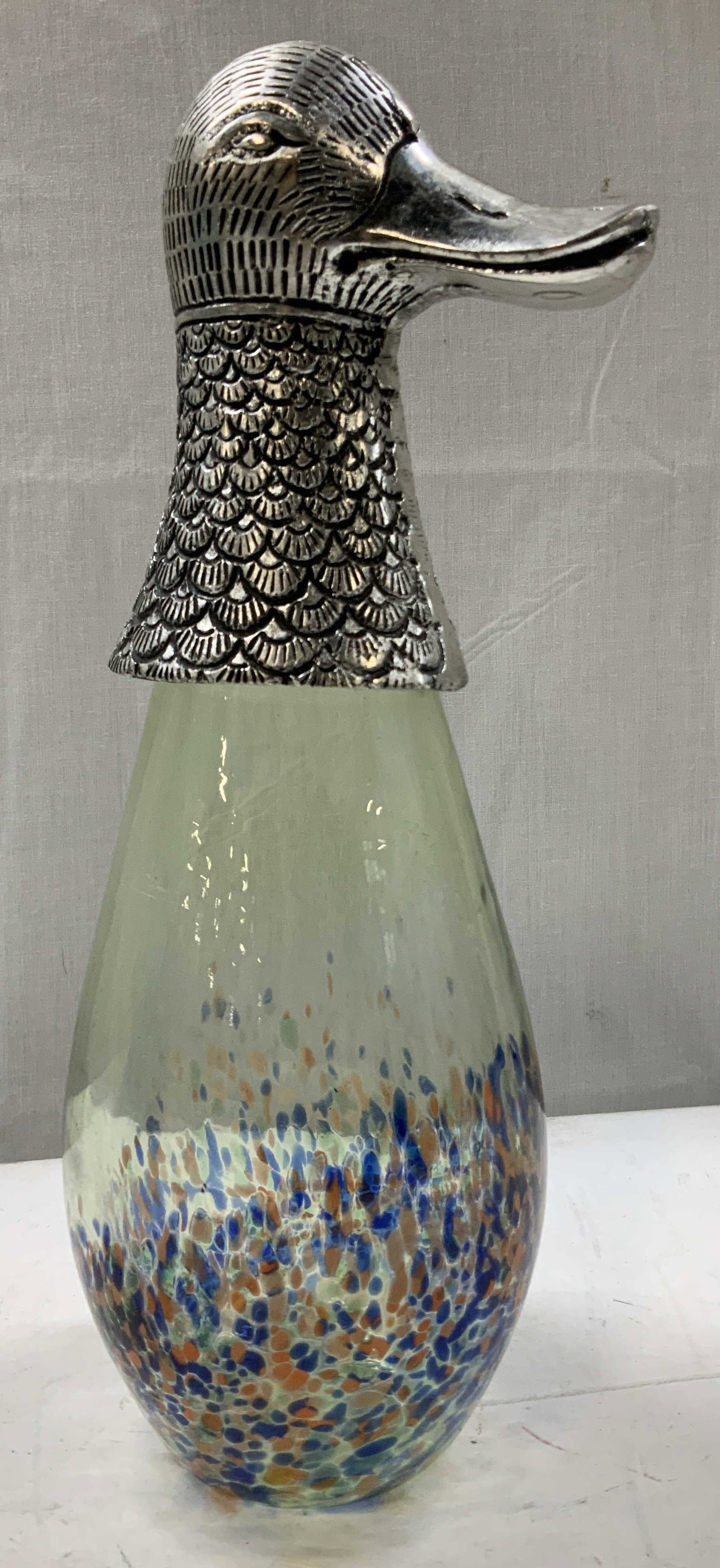 Speckled Art Glass Metal Duck Figural: Art glass figural features a silver-toned textured duck head perched on a tear drop shaped glass body. Glass body has multicolored speckles in blue, orange & green tones. No visible signature or marki