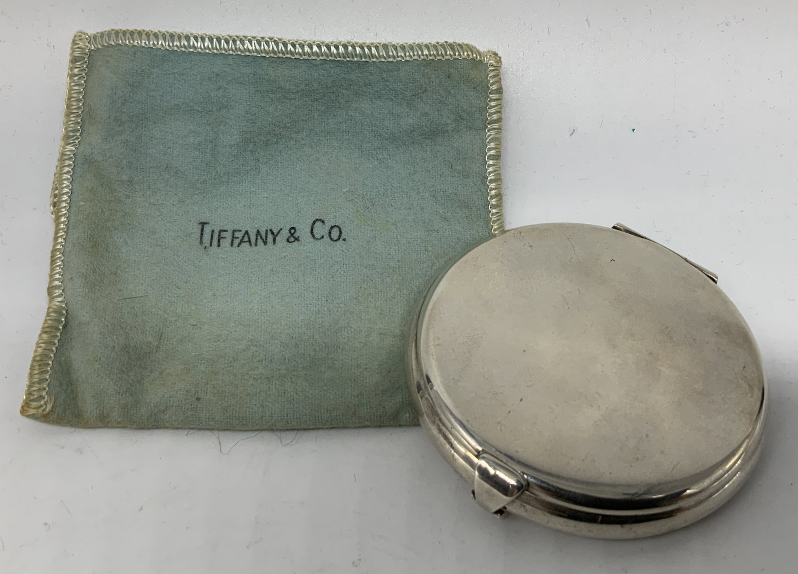 Tiffany & Co. Sterling 2.87 OZT Powder Compact: Powder compact is sterling & weights 2.87ozt. Interior features a mirror & an empty powder compartment below. Comes with Tiffany & co. cloth pouch. Surface wear consistent to age, use & exposure. Meas