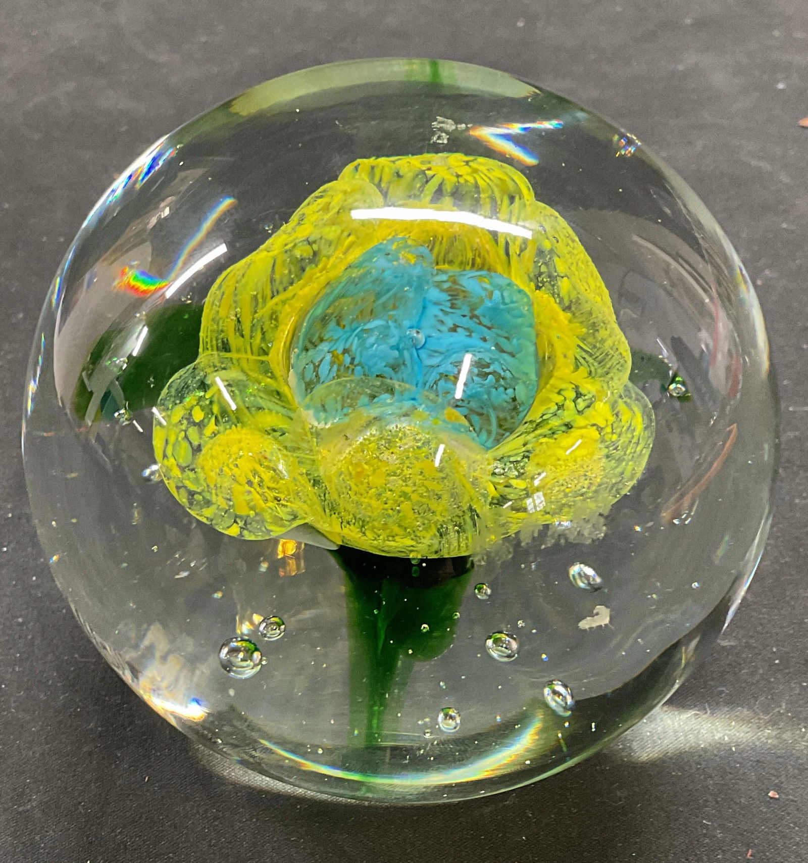 Hand Blown Art Glass Flower Paperweight: Hand blown art glass paperweight. Flower design. Clear glass with yellow, blue, and green inclusions. Measures approx 3.5 x 3.5 inches. Minimal surface wear. Art glass paperweight, flower paperweight,