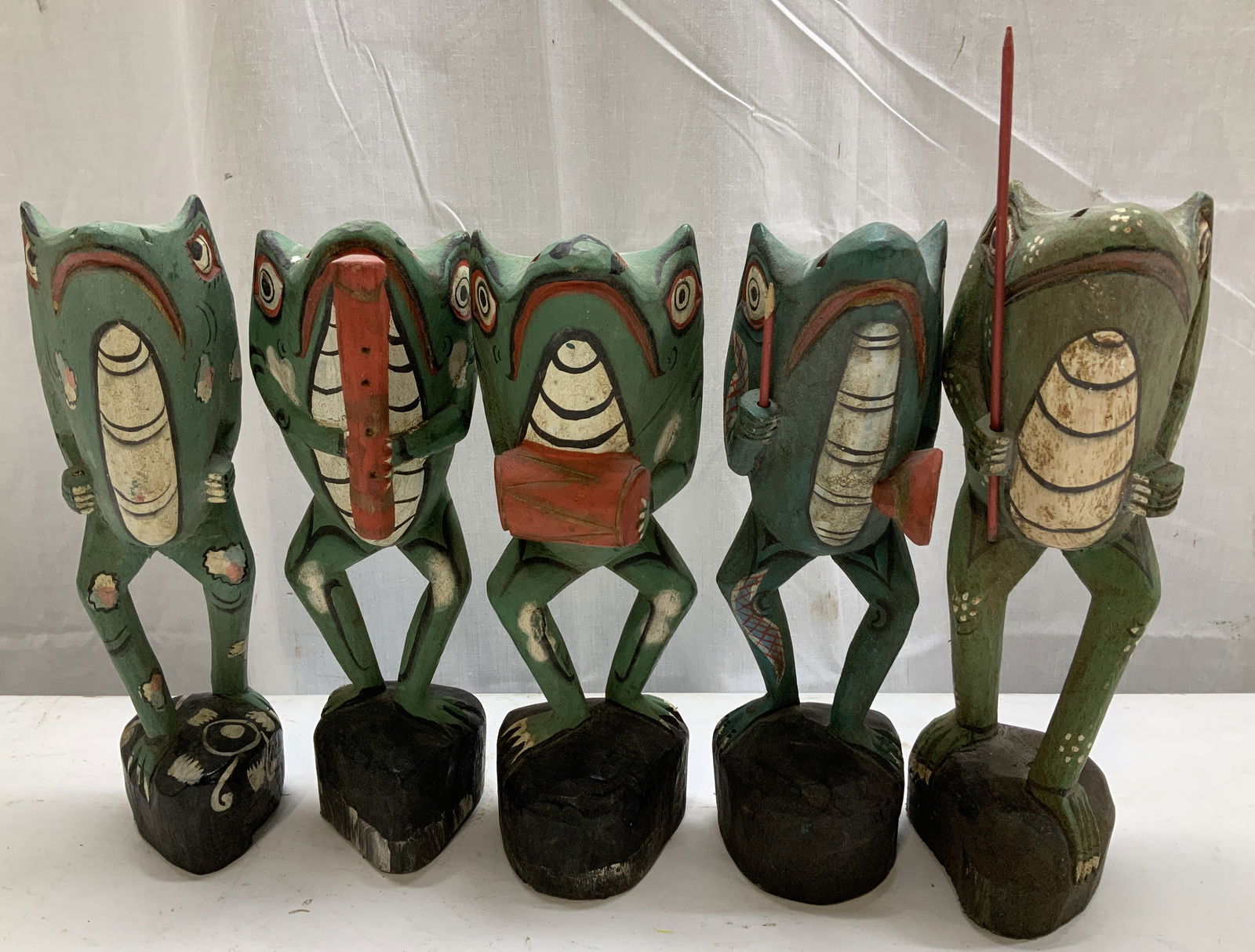 Set 5 Hand Carved Musical Band Frog Figurines: Whimsical group of hand-carved & hand-painted wooden frog figures. Each figure is standing upright & 4 are holding musical instruments. Elongated bodies & are mounted on a black wooden base. No visibl
