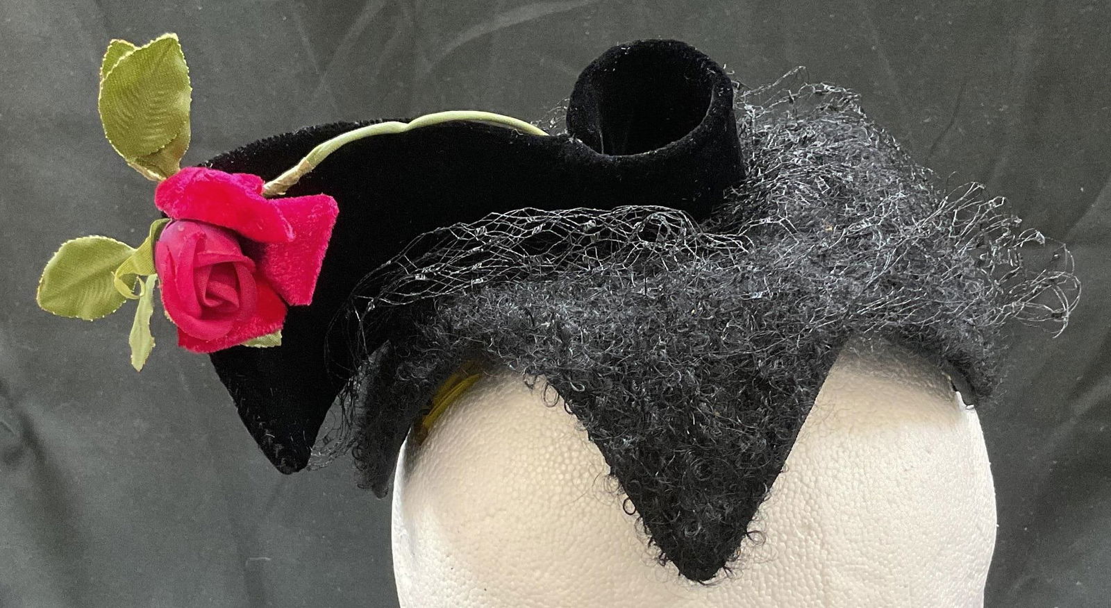 Agnes Black Rose Mesh Fascinator: Agnes black rose mesh fascinator. Feels like wool. Structured base with what feels like mesh. Adorned with black velvet bow with red and green rose detailing. Measures approx 8 inches wide. Detaching