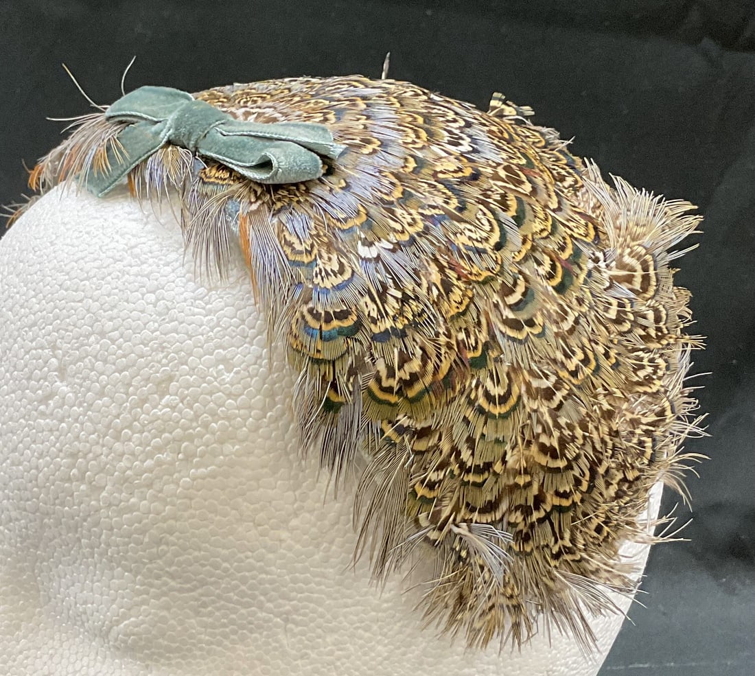 Vintage Blue Feathered Fascinator: Vintage blue feathered fascinator. Feels like wool. Feather design in blue, brown, white, black, and more. Features blue velvet bow. Underside has scalloped gold toned trim. Measures approx 11 inches