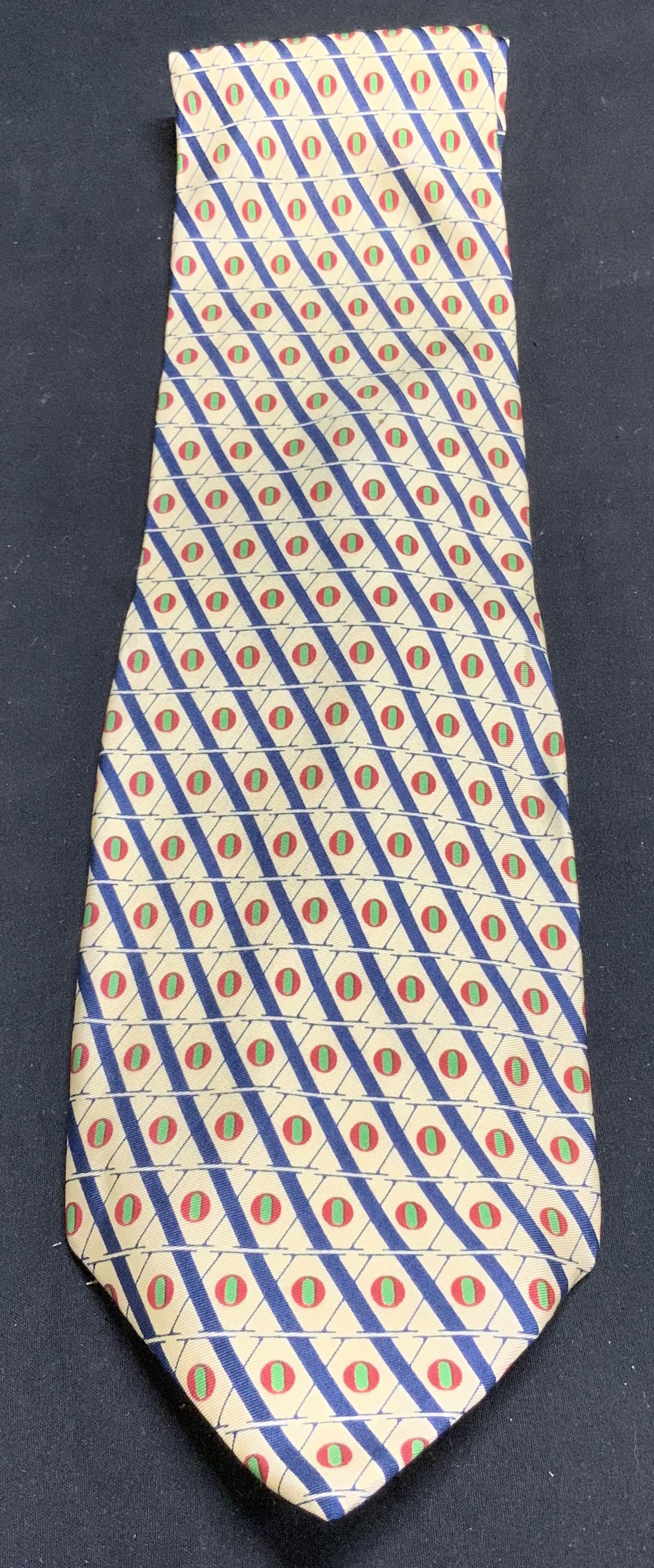 MOSCHINO Yellow Geometric Silk Necktie: Necktie is silk & features a repeating X pattern with red oval & green details. Signed & marked. Reads, MOSCHINO. Surface wear consistent to age, use & exposure. Measurements: length 57.6in x width 4i