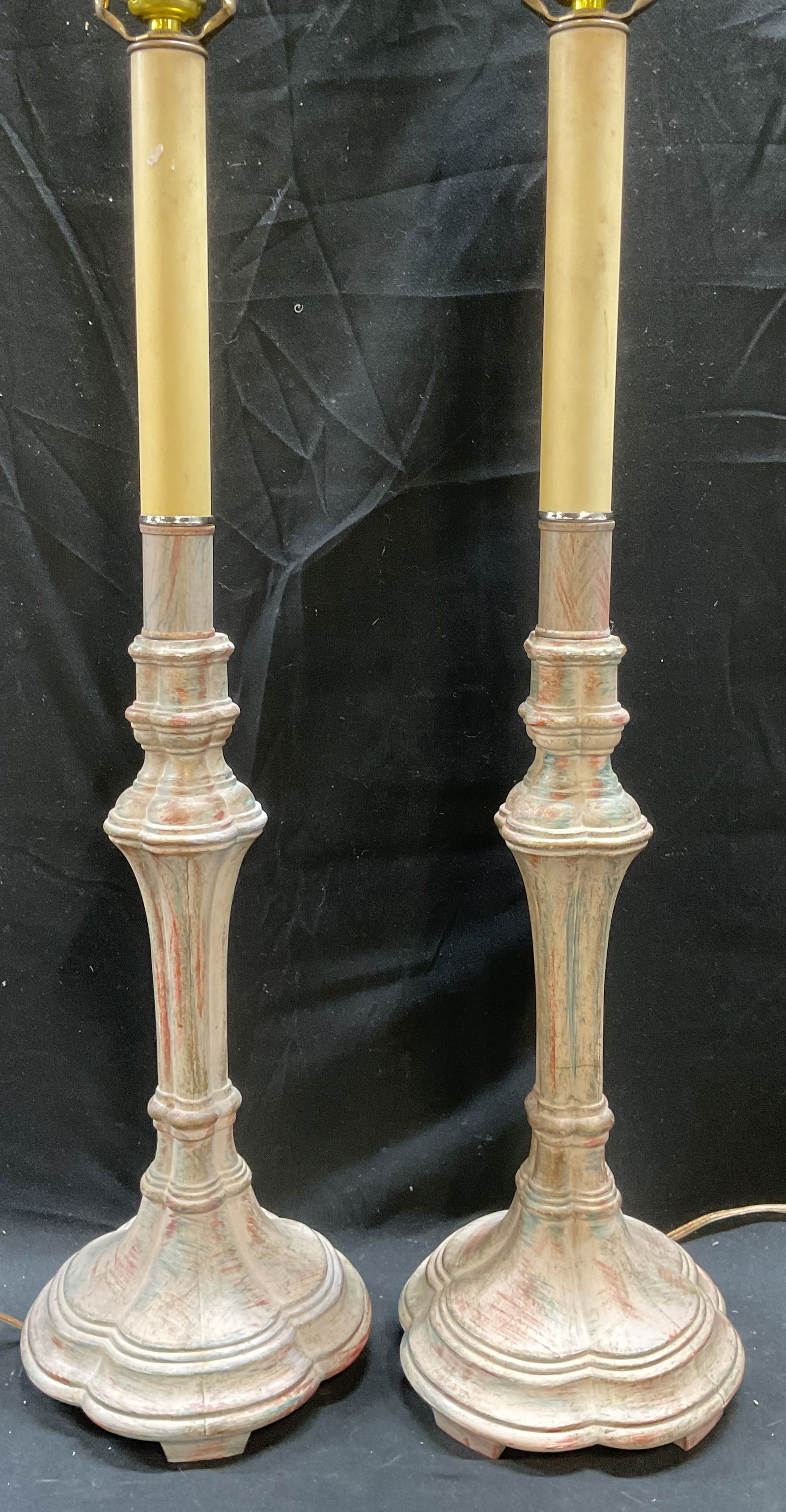 Pair Enameled Metal Candlestick Motif Lamps: Pair of off white enameled metal table lamps with candlestick motif design. Decorative columns and bases. Measure approx 6.5 x 21 inches excluding harps. Some scratching. One foot needs repair. Not te